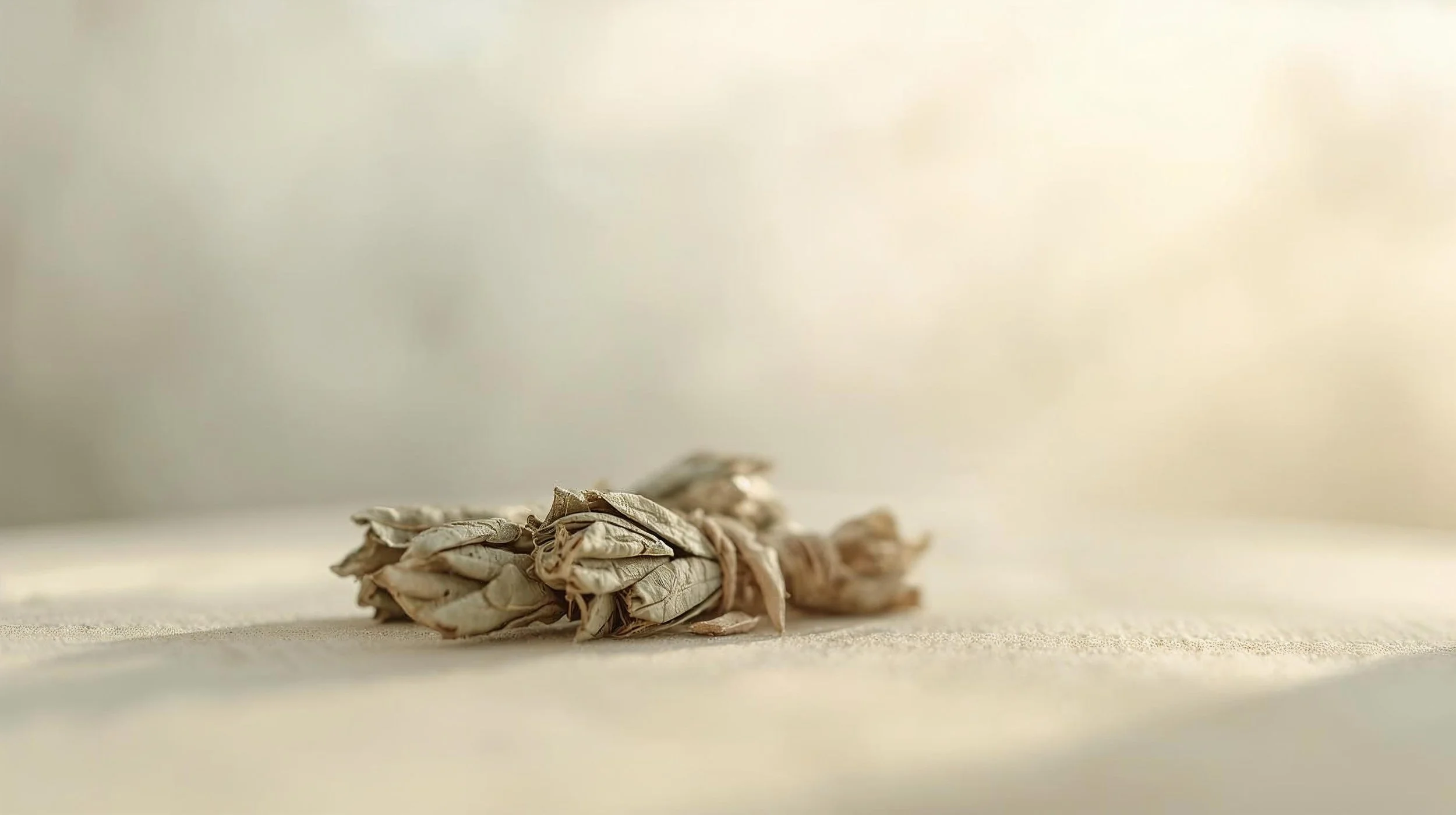 A bundle of dried, crumpled sage leaves tied together with a string, resting on a light-colored surface.