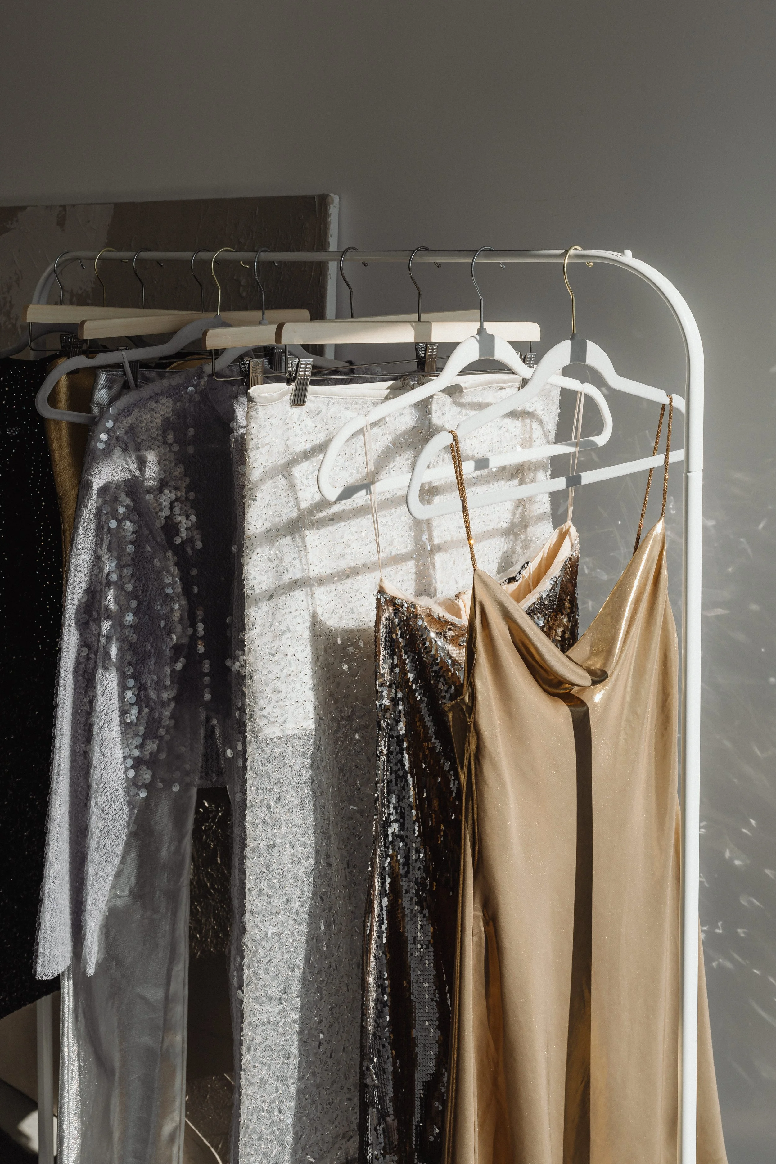Clothing rack with various sparkly and metallic dresses, including black, silver, and gold, hanging on hangers.