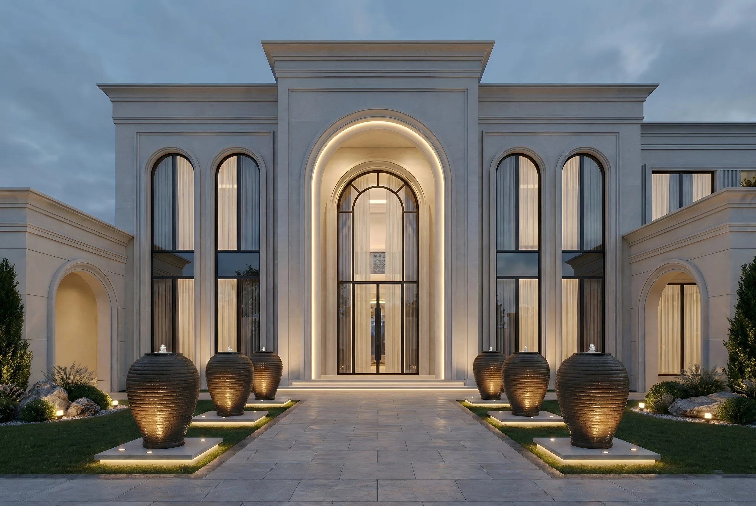 Front of a large, luxurious mansion with illuminated exterior lighting, tall arched windows, and decorative urns lining the walkway.