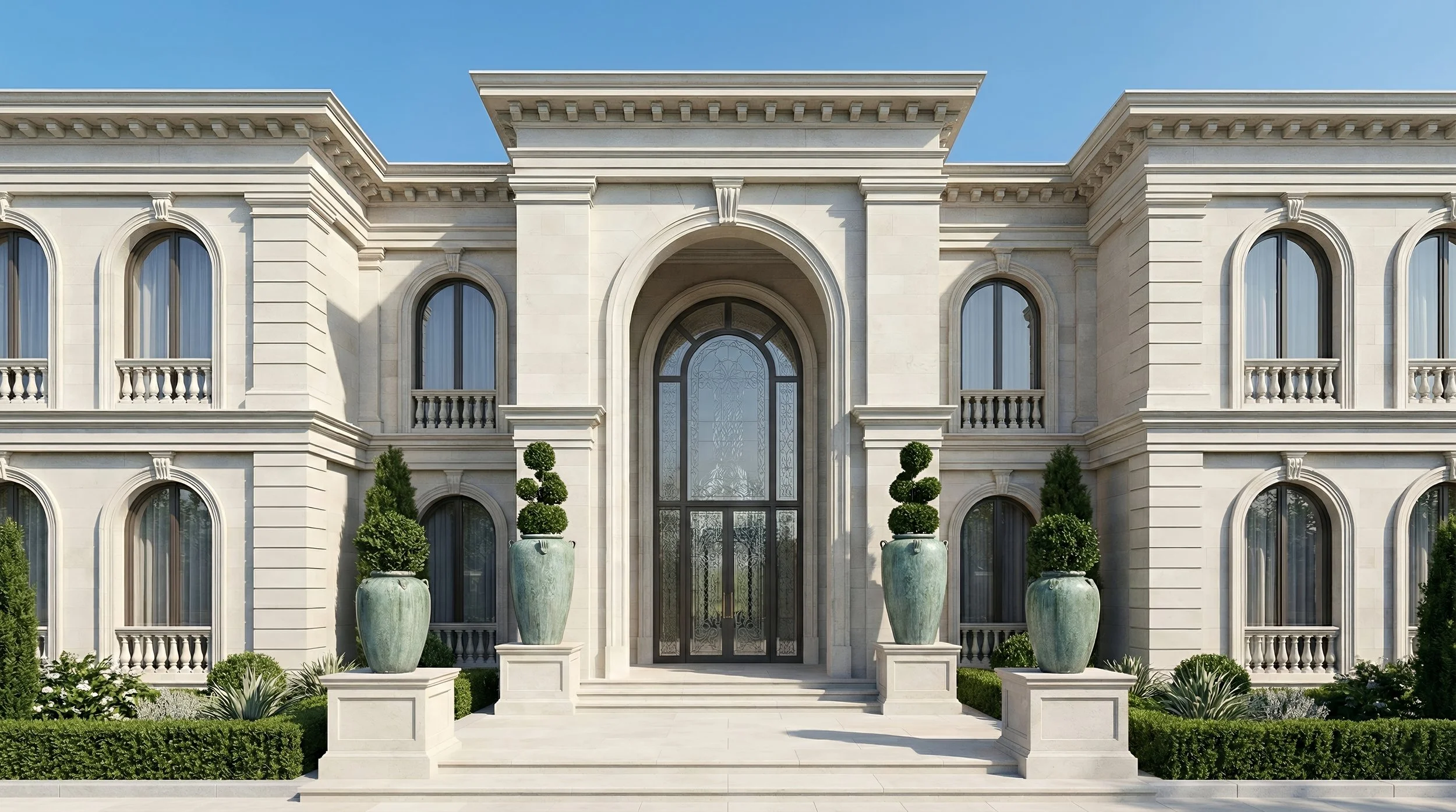 Front view of a grand, classical-style mansion with large arched windows, decorative columns, and potted topiary plants on pedestals at the entrance, under a clear blue sky.