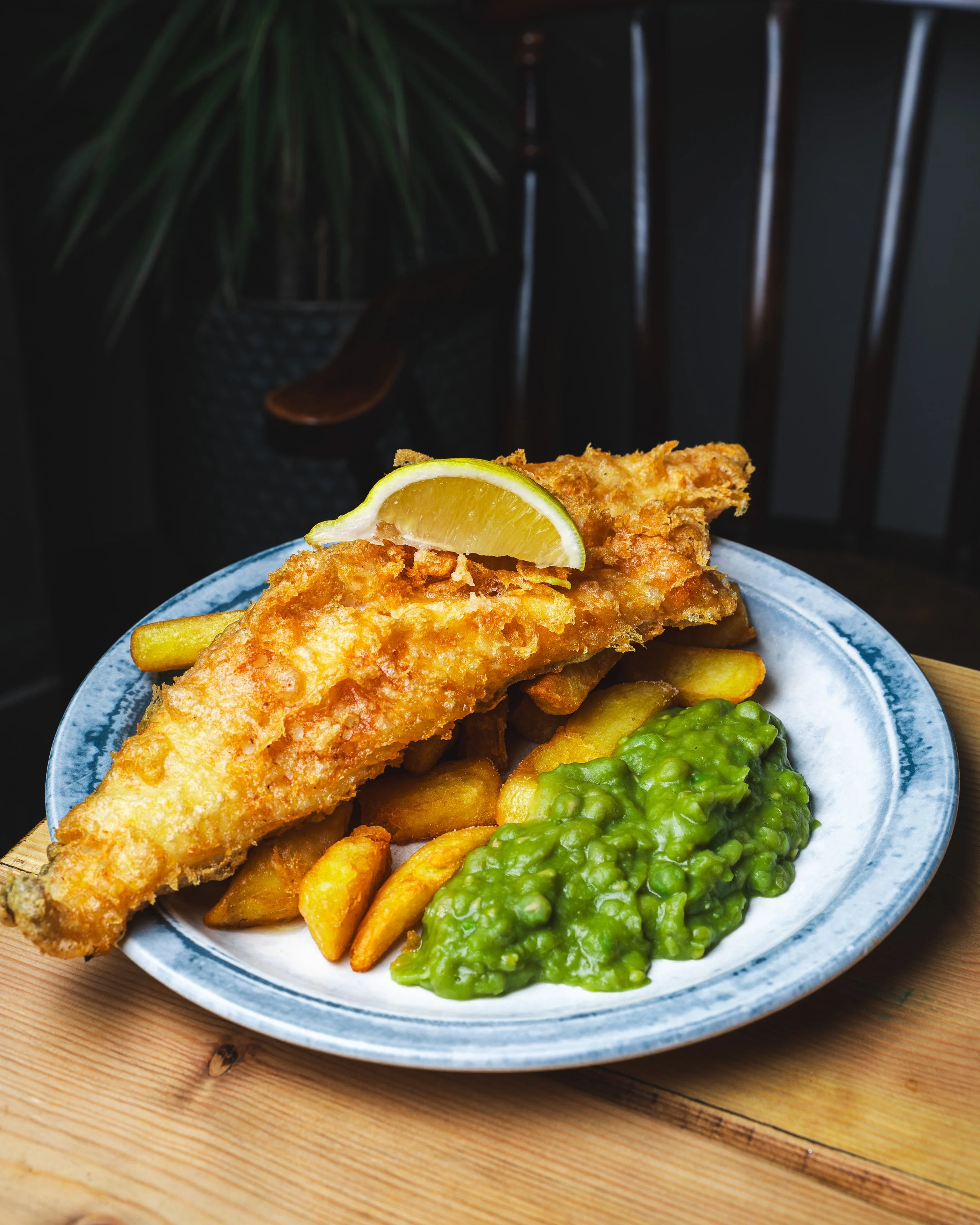 Fried fish fillet served with lemon wedge, potato fries, and green peas on a blue-rimmed plate.