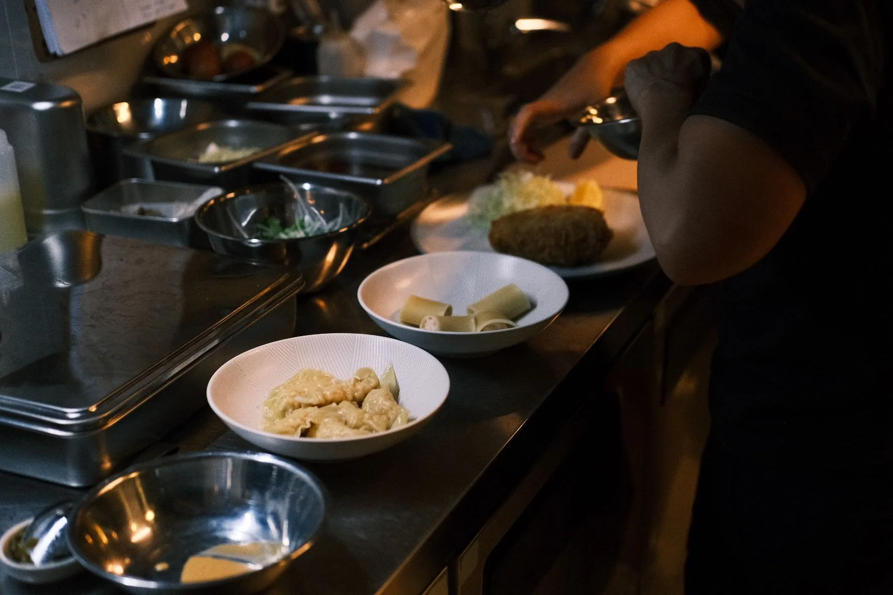 Person preparing food in a professional kitchen, with bowls of ingredients on a stainless steel counter.
