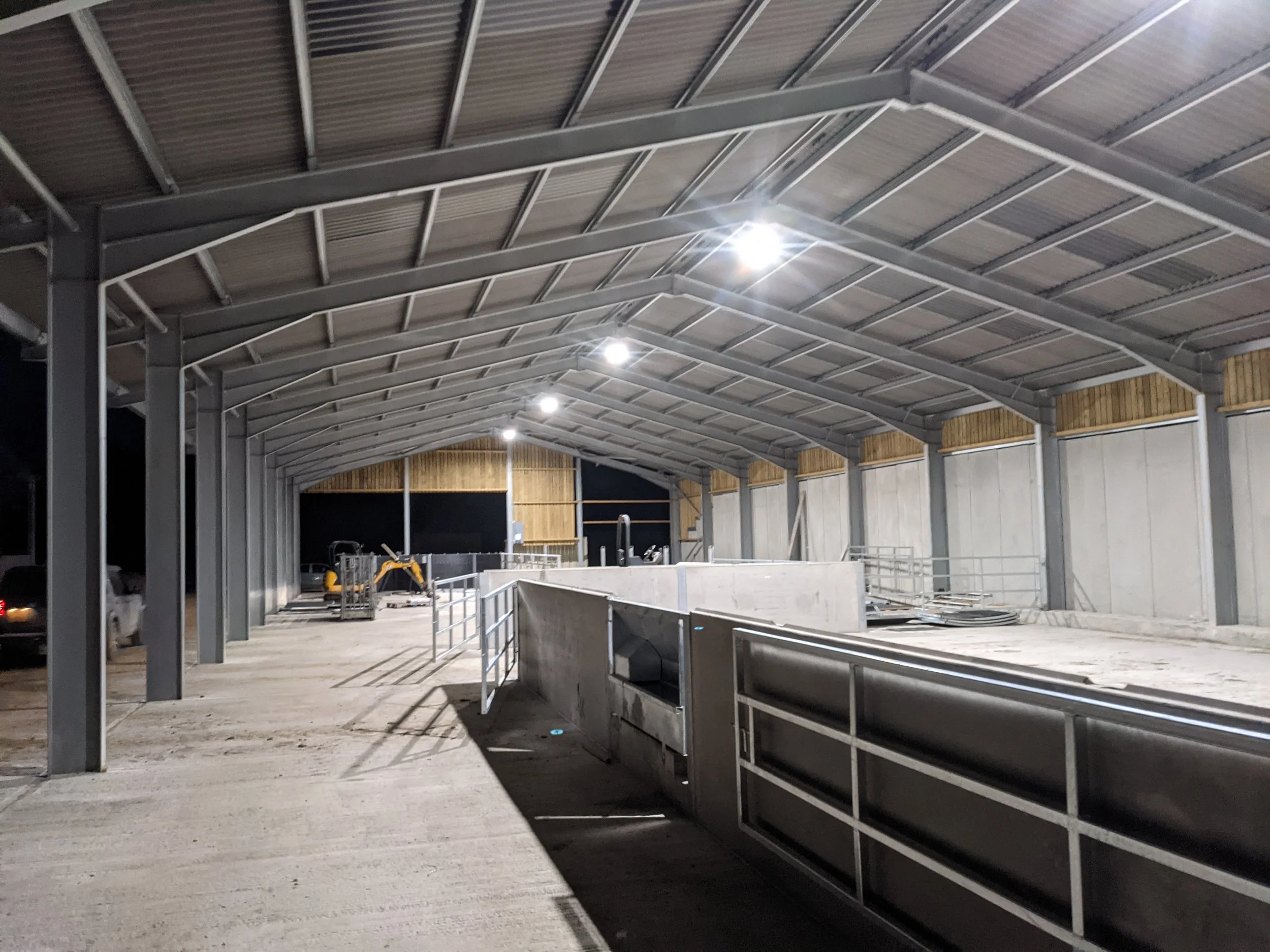 Interior of a covered structure under construction with metal framework, lighting, and construction equipment.