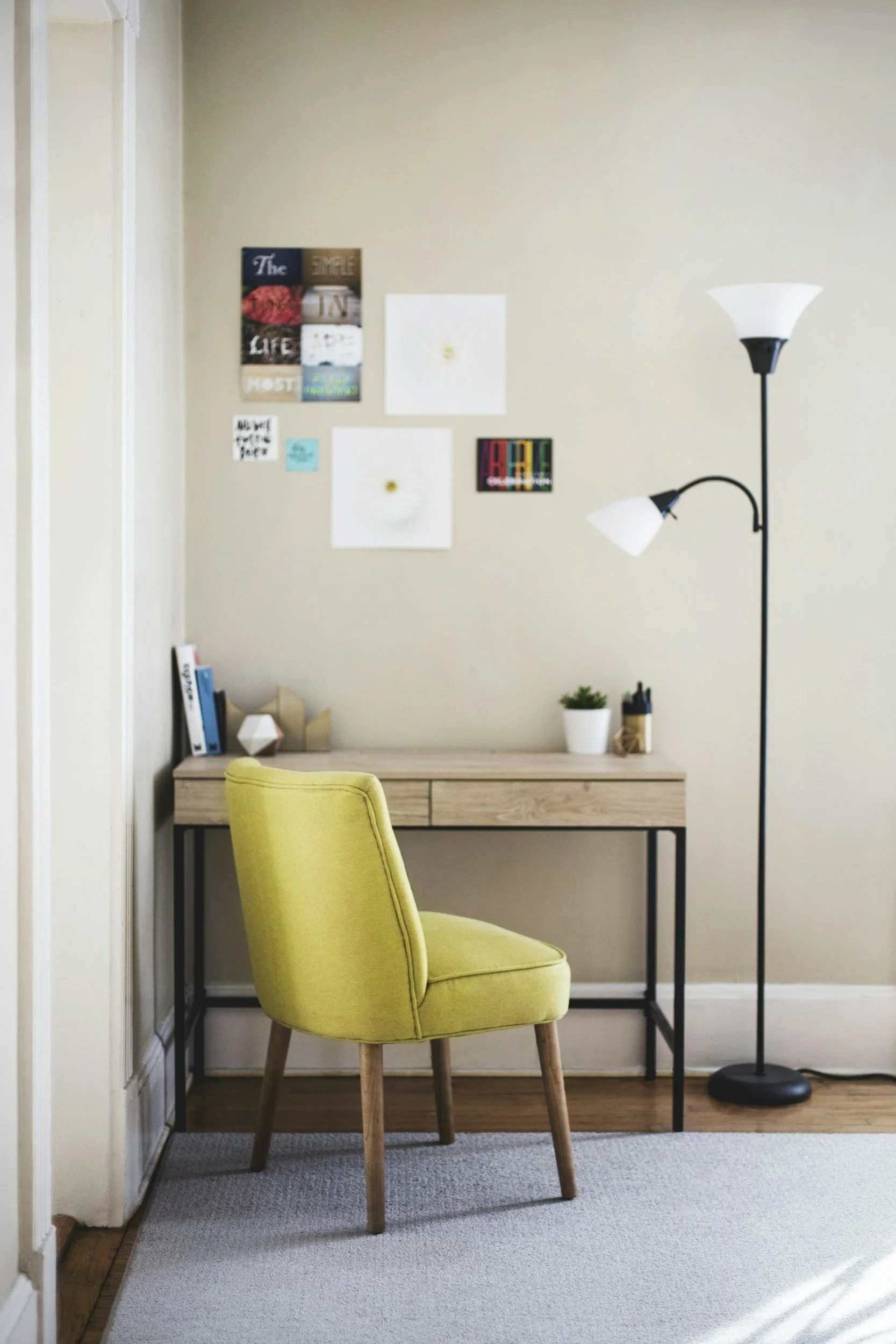 Home office with a yellow chair, wooden desk, potted plant, wall art, and a black floor lamp.