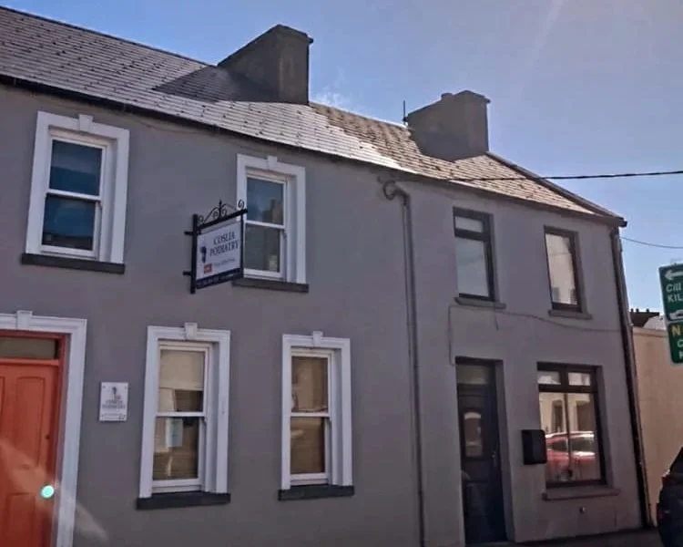 A two-story gray building with white-framed windows, located on a street corner. Coslia Podiatry Kilrush clinic on Vandeleur Street, Kilrush, Co. Clare
