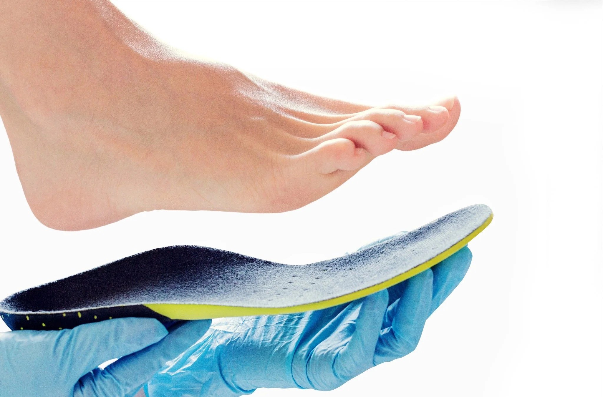 A foot hovering above a shoe insole held by a person wearing blue gloves. Medical orthotics.