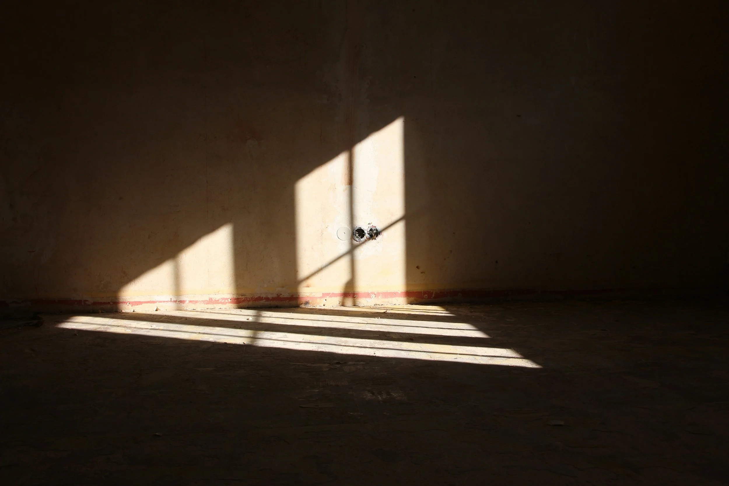 Sunlight streams through a window of a upcoming renovation, casting shadows on an empty, unfinished wall and floor in a room under construction.