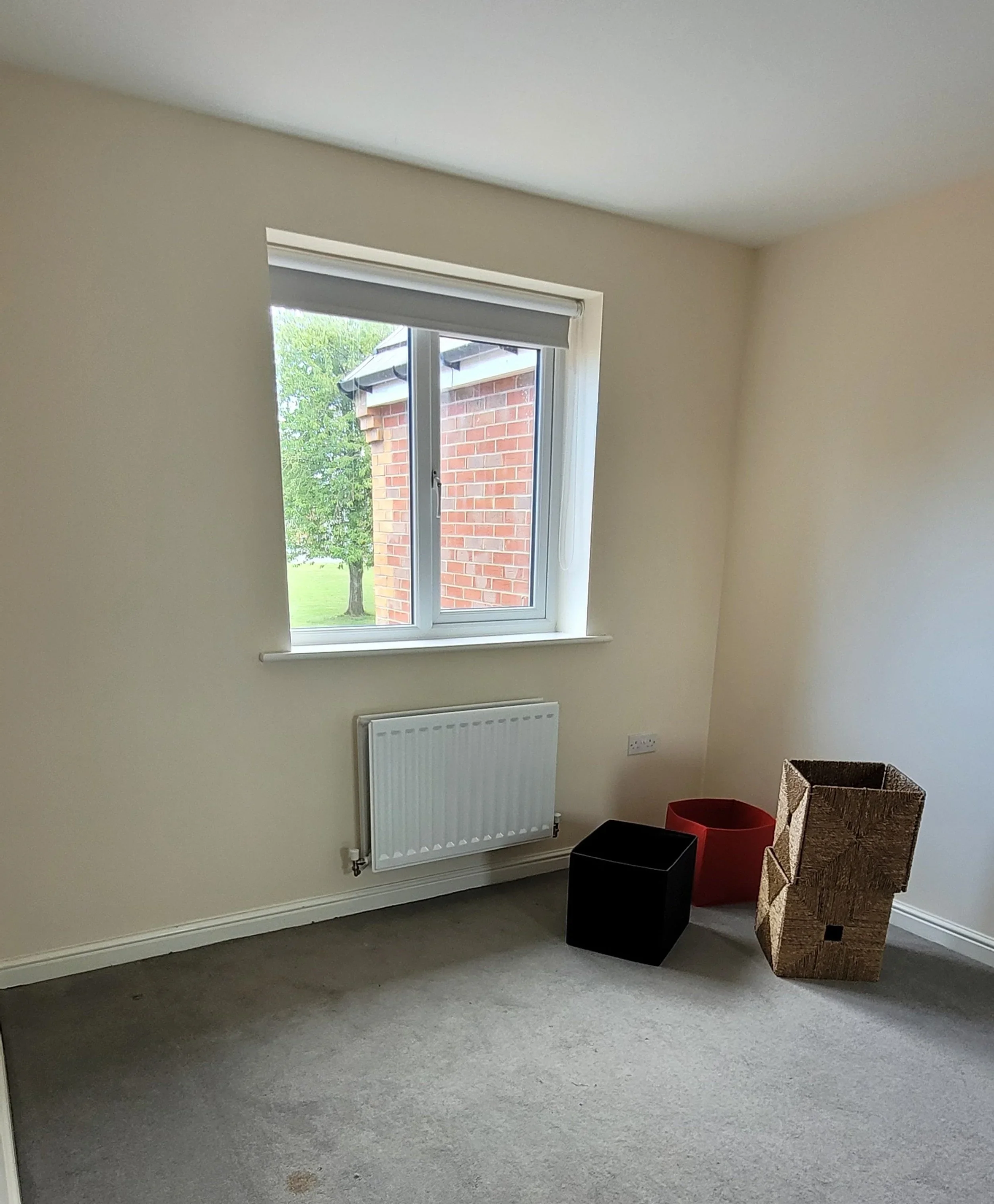 Empty room with a window, radiator, and three storage boxes near the corner.