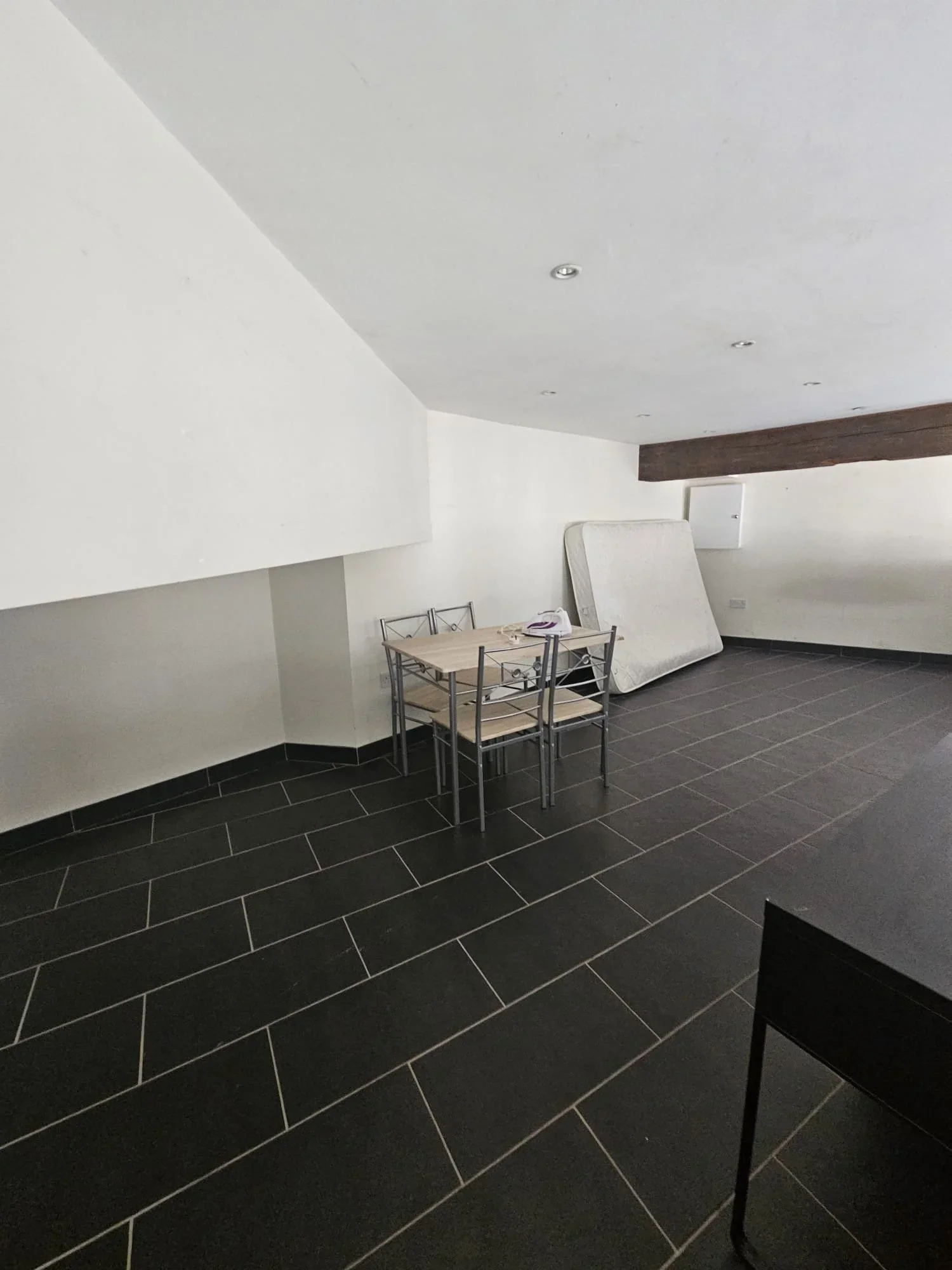 Empty room with black tile flooring, a small table with chairs, and a folded mattress against the wall.