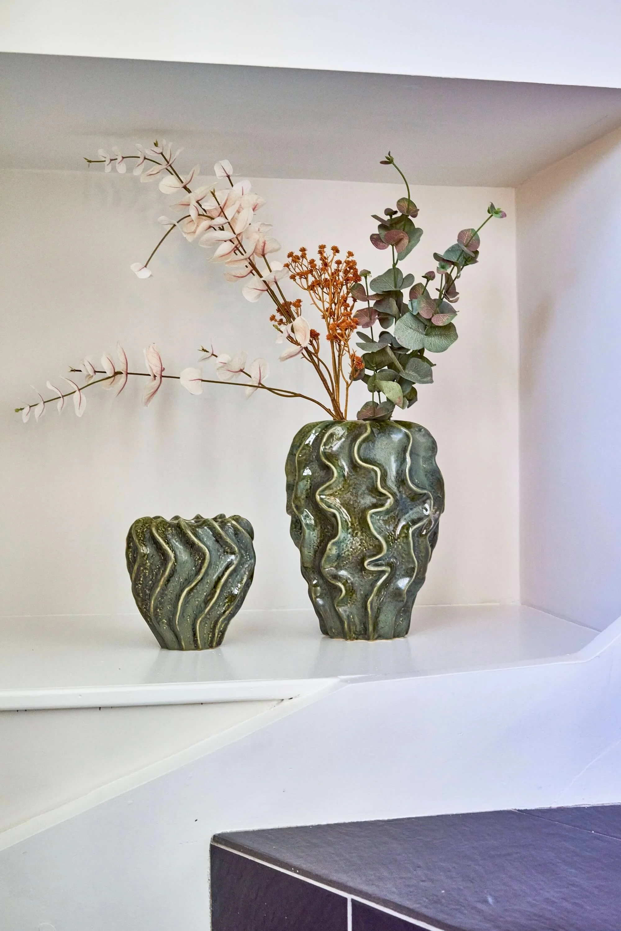 Decorative vases with floral arrangements on a white shelf.