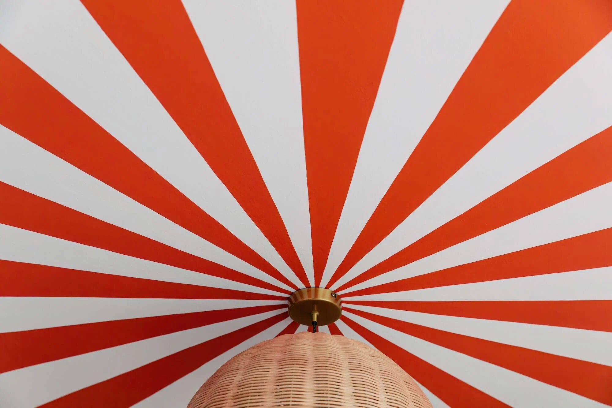 View of a ceiling with a red and white radial striped pattern and a hanging woven light fixture in the center.