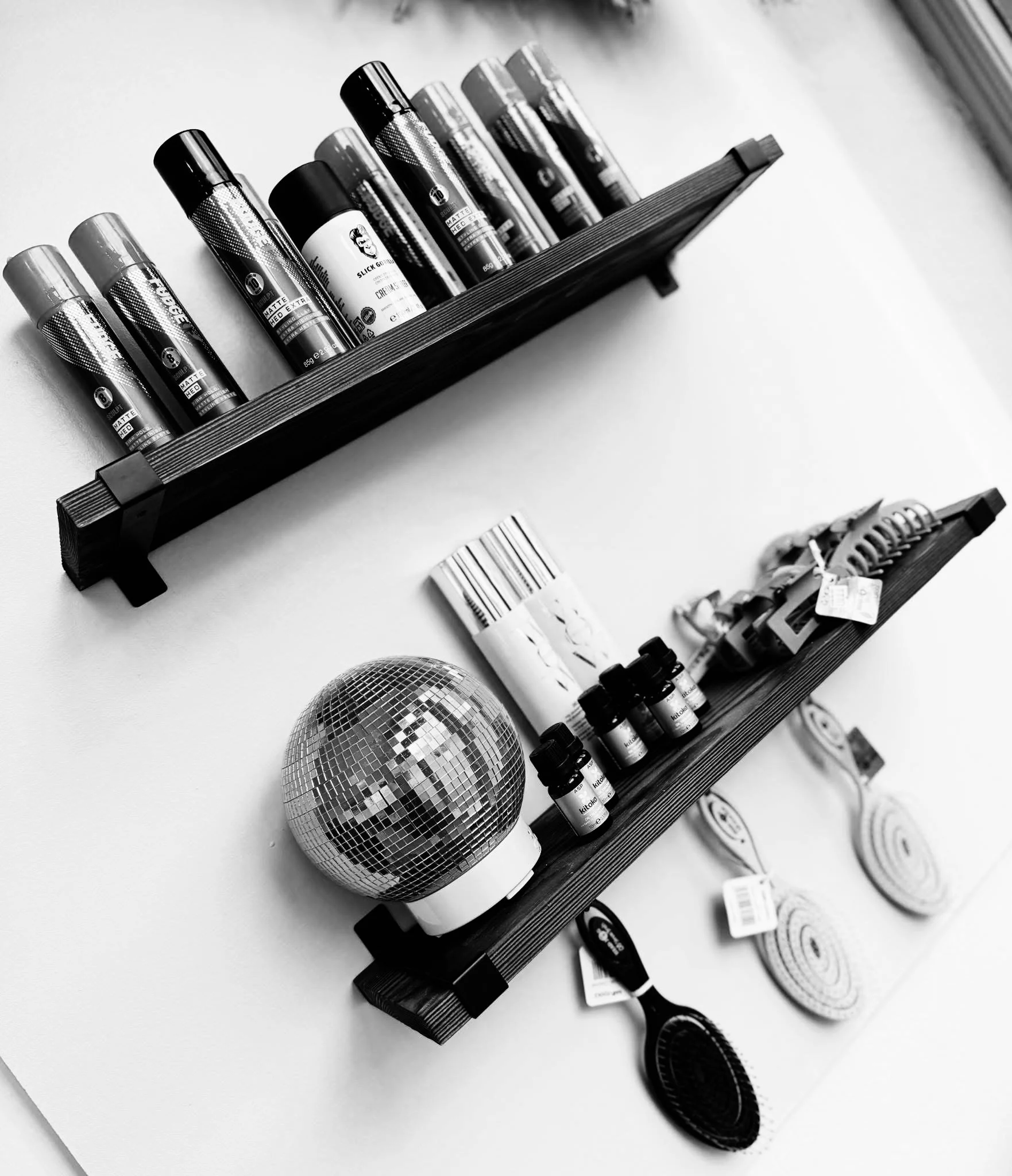 Two black shelves mounted on a wall holding various skincare and beauty products, including creams and small bottles. The scene also includes a disco ball, three coiled objects, a small brush, and a few other miscellaneous items.