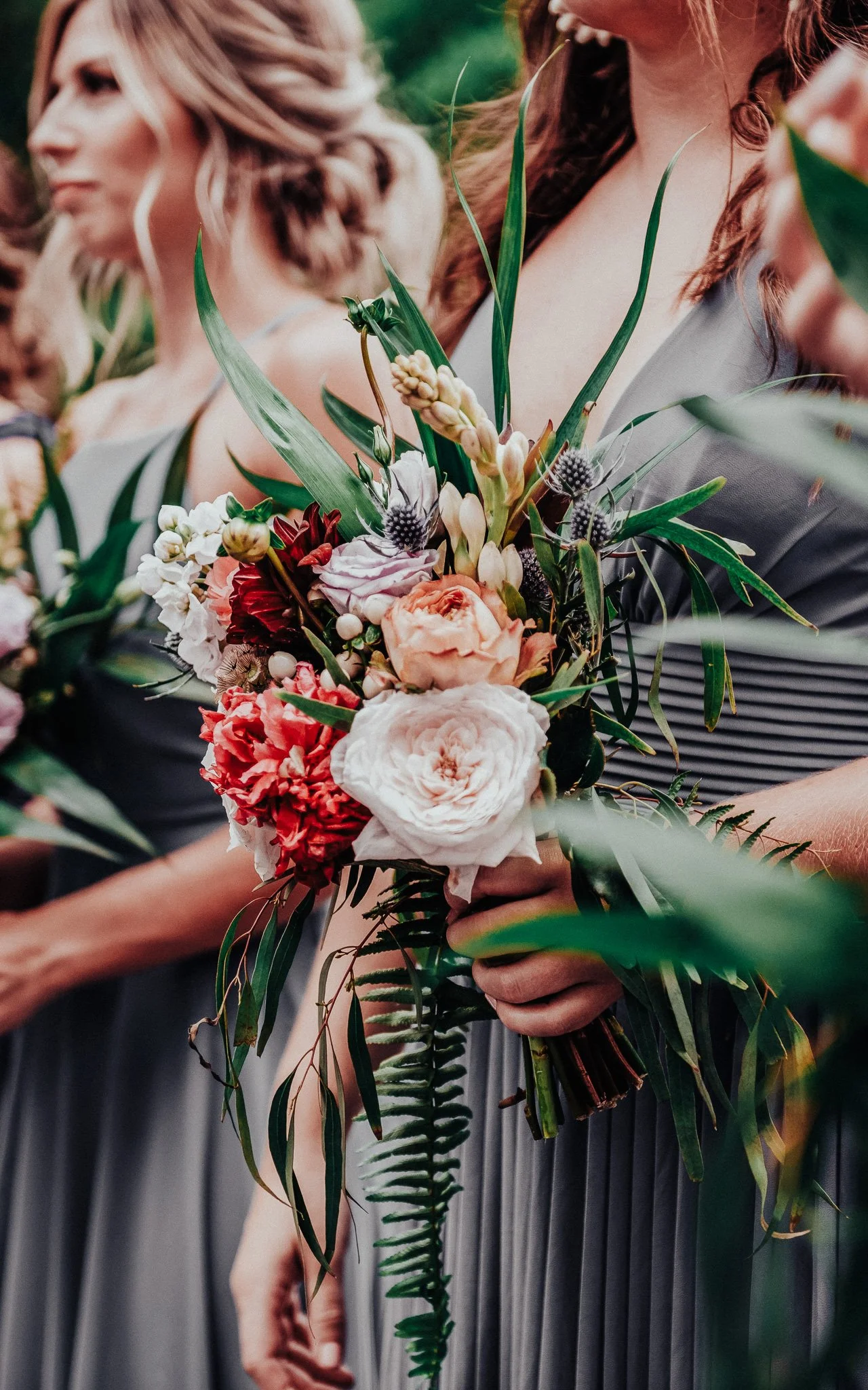 Nahaufnahme von Frauen in eleganten Kleidern, die bei einer Zeremonie einen Blumenstrauß halten.