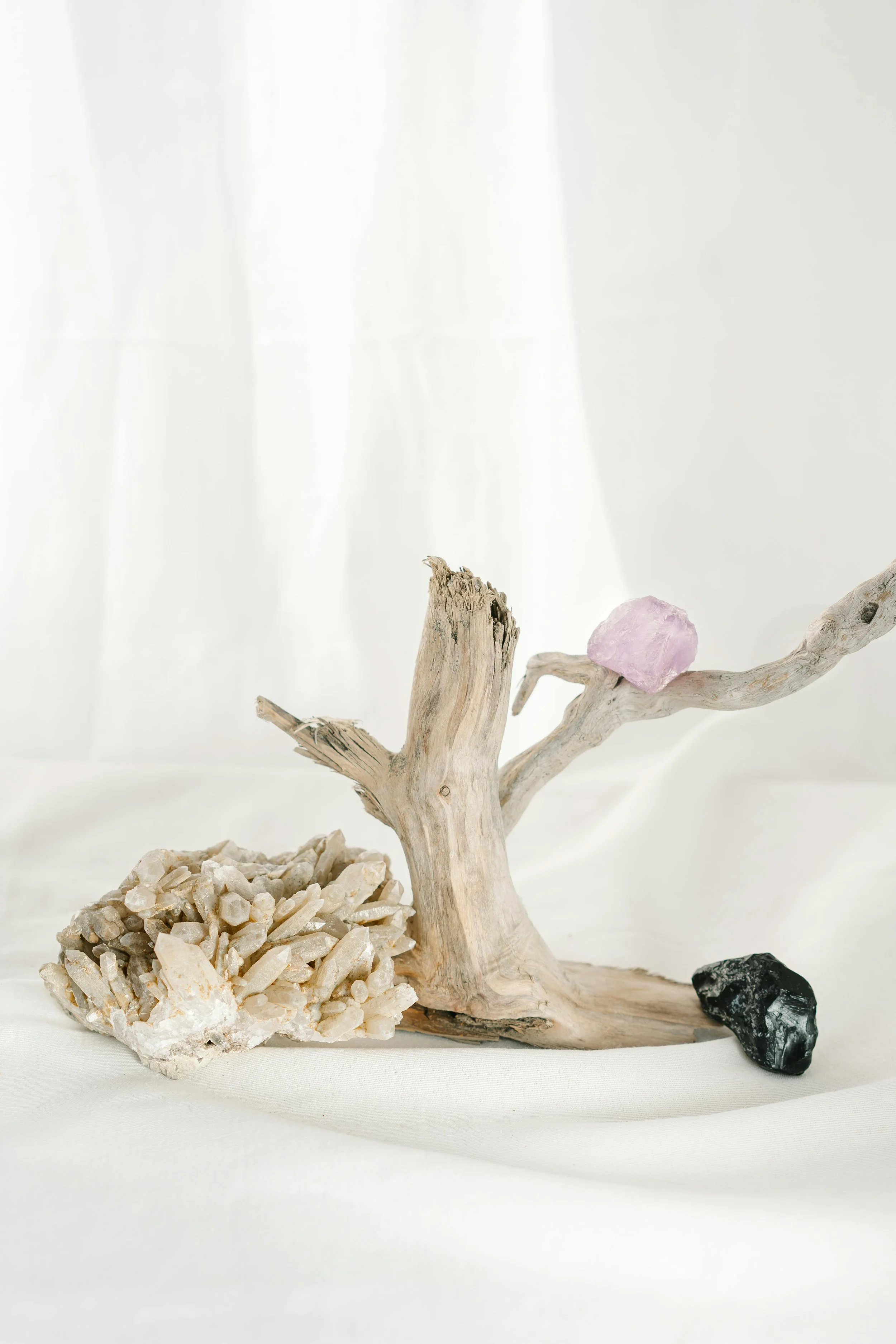 Arrangement of rocks and driftwood with a purple gemstone on a white soft surface.