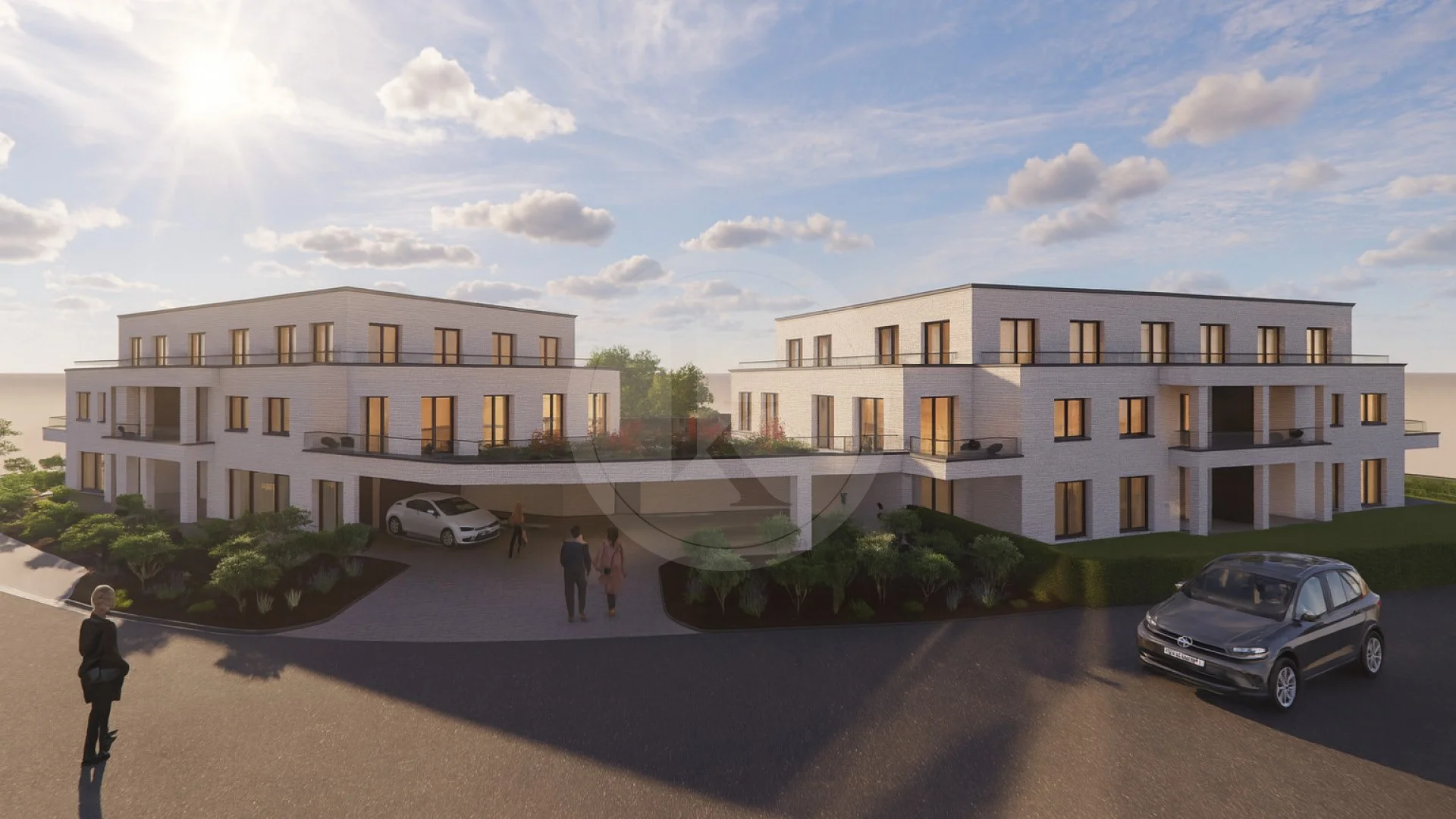 Ein modernes Wohngebäude mit zwei Stockwerken, weiße Fassaden, viele Fenster und Balkone, im Vordergrund eine Auffahrt mit Autos und Fußgängern, umgeben von kleineren Büschen und Bäumen, bei sonnigem Himmel mit wenigen Wolken.