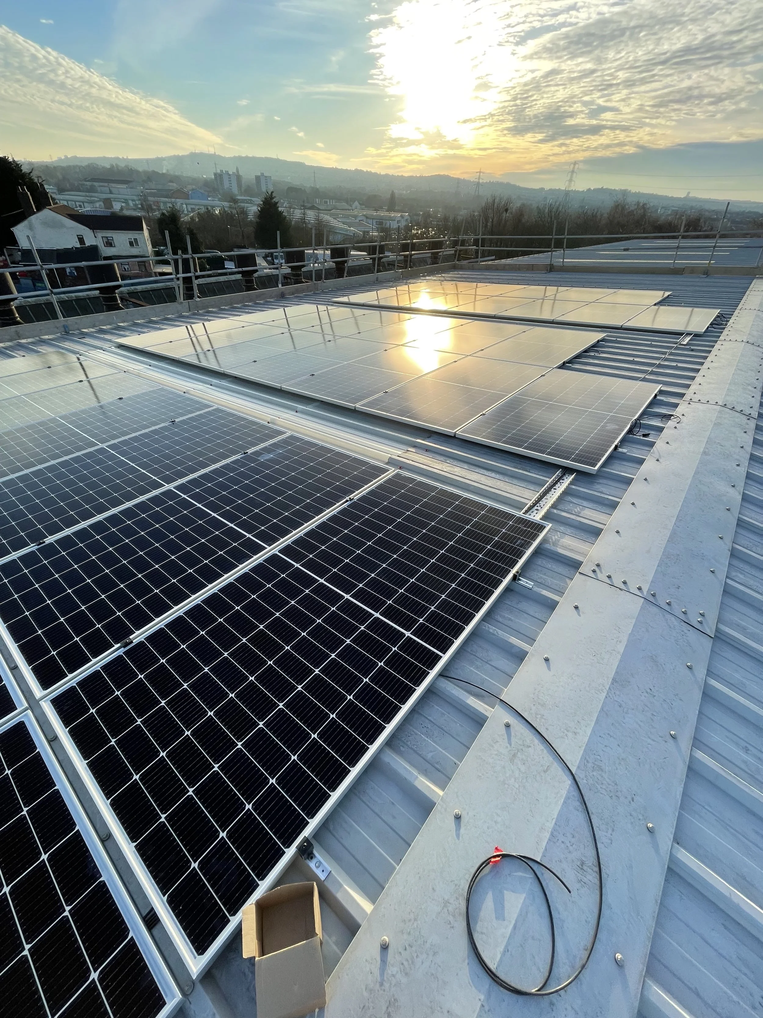 Solar panels installed on a metal rooftop at sunset with a city skyline in the background.
