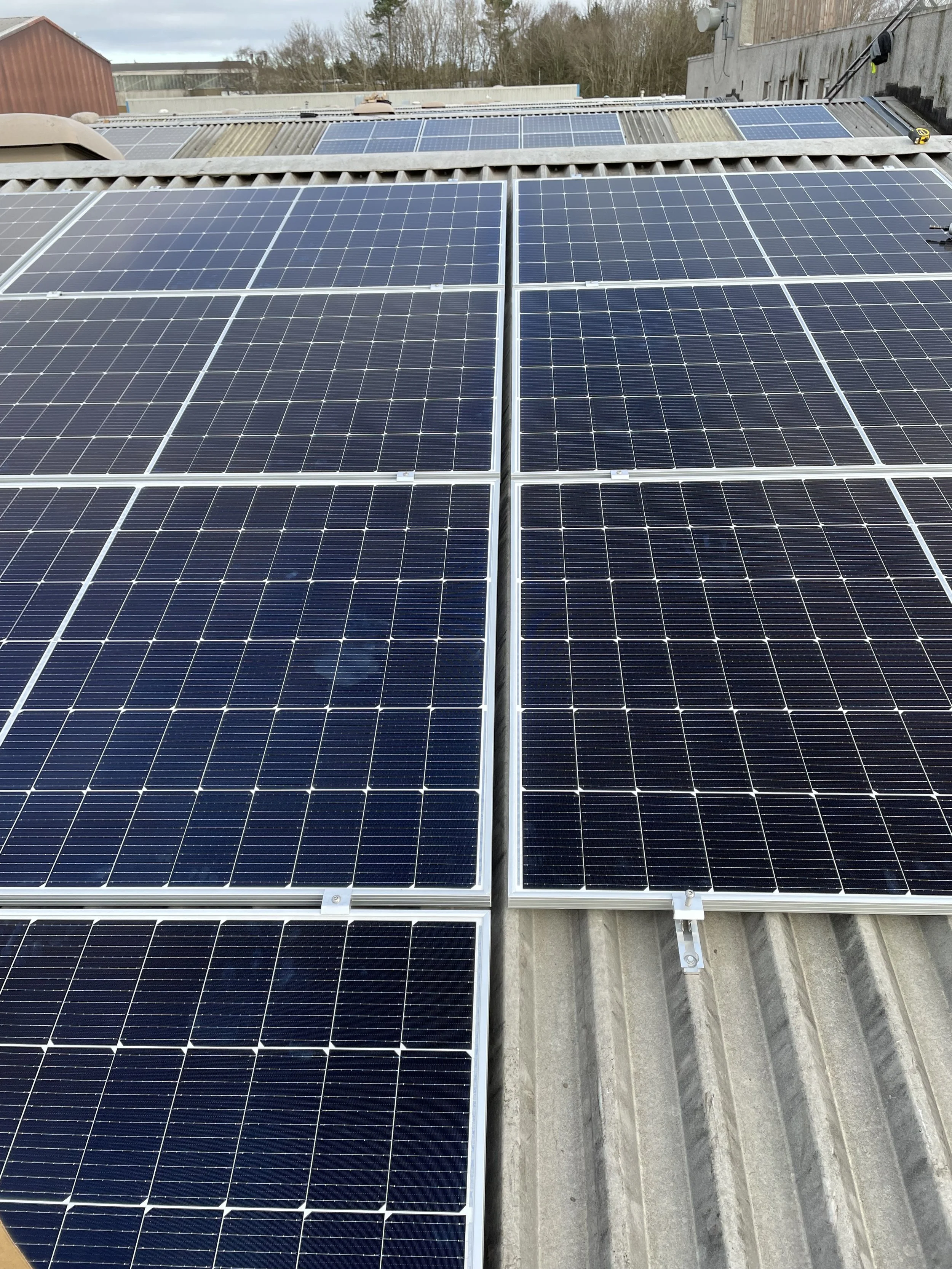 Multiple solar panels installed on a roof with a cloudy sky in the background.