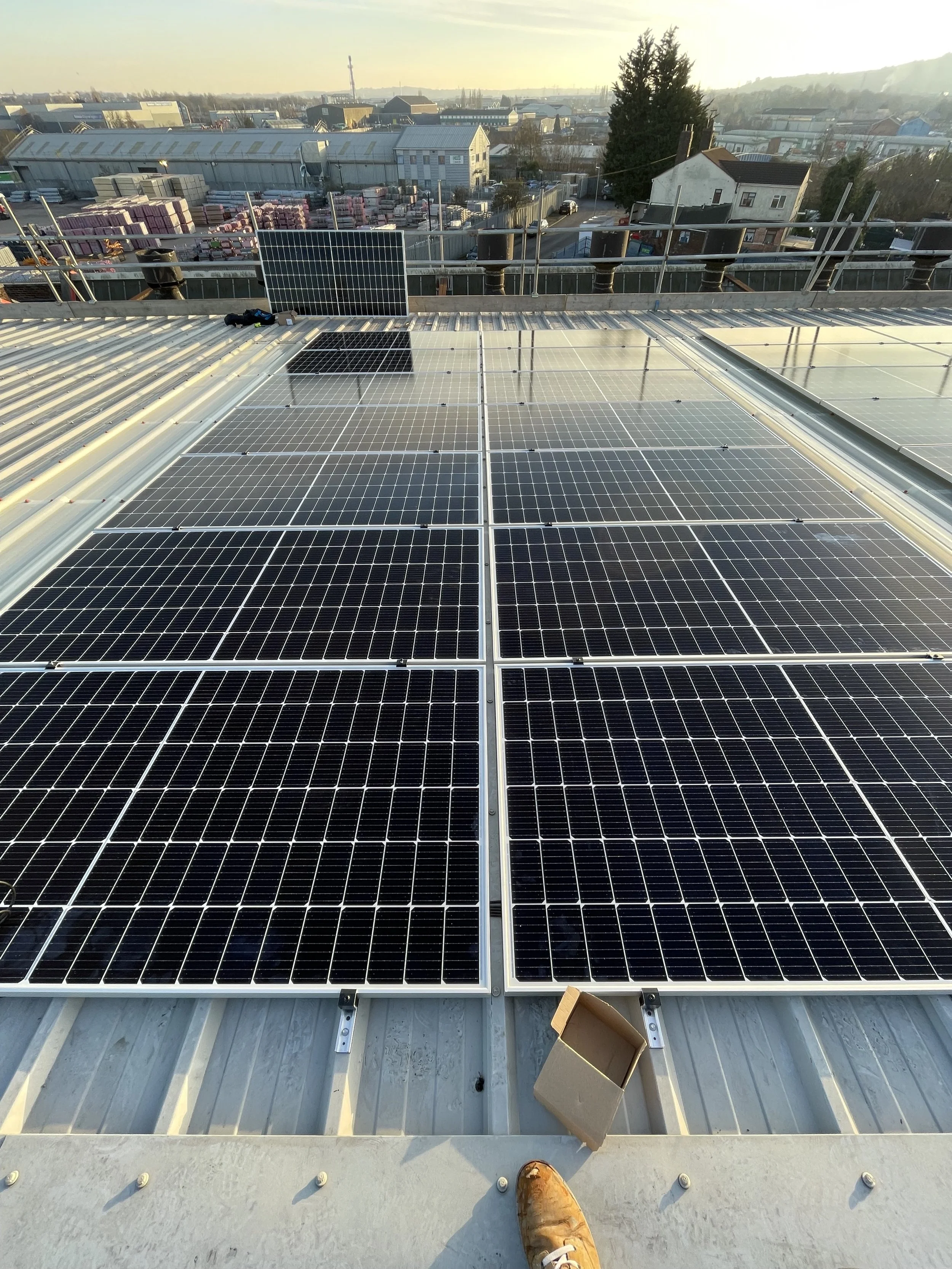 Multiple solar panels installed on a rooftop with surrounding buildings and a distant cityscape under a clear sky.
