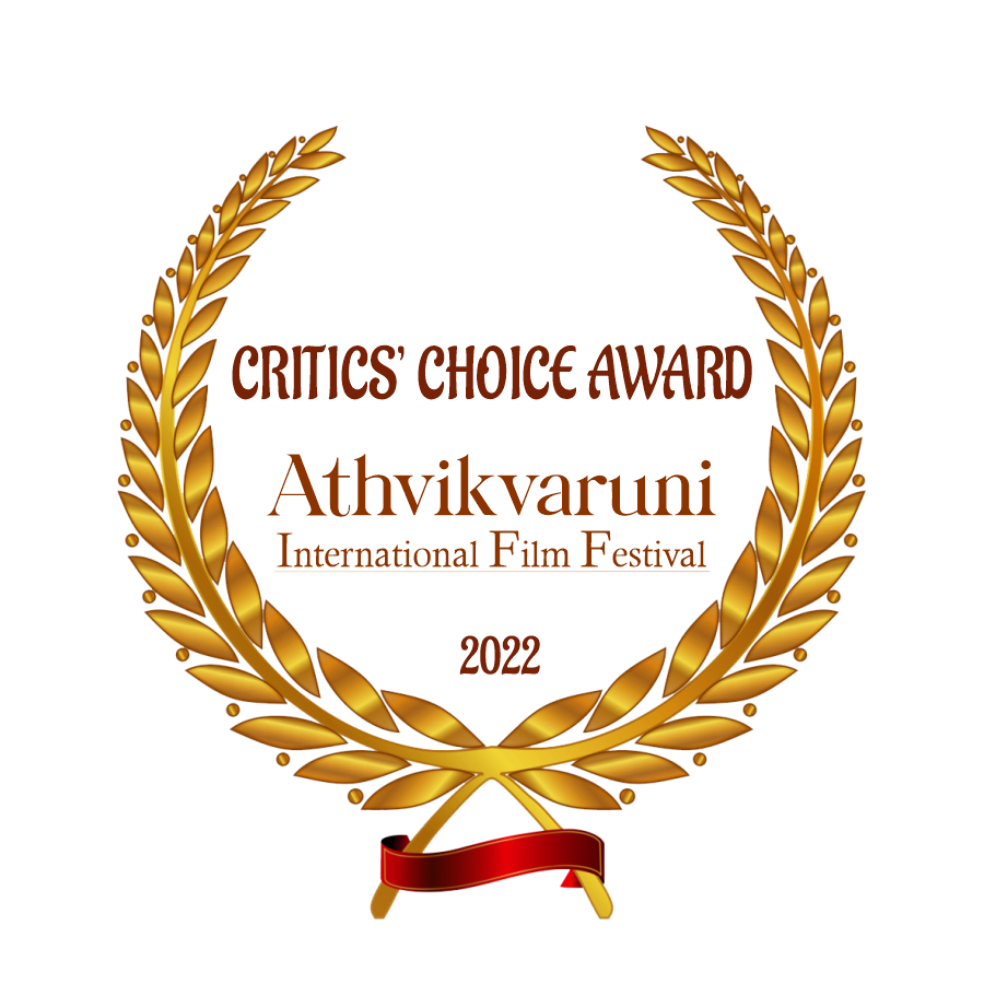 A gold laurel wreath with a red ribbon at the bottom. Inside, the text reads: " Critics' Choice Award, Athvikvaruni International Film Festival, 2022," indicating an award from a film festival.