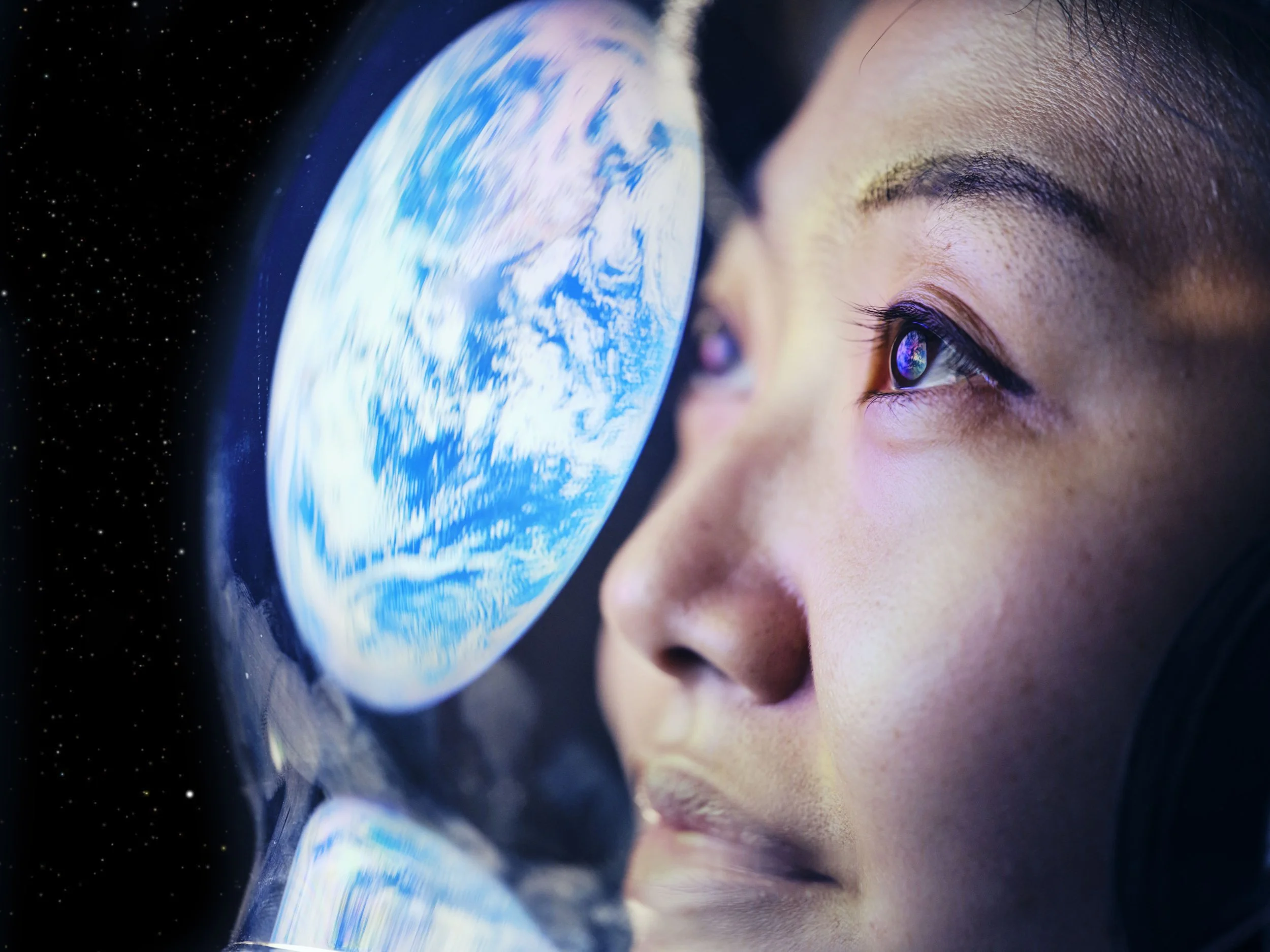 Close-up of a woman's face looking at Earth through a telescope, with space and stars in the background.