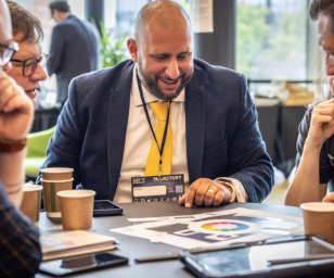 Group of business professionals engaged in a discussion at a conference table with coffee cups and presentation materials.