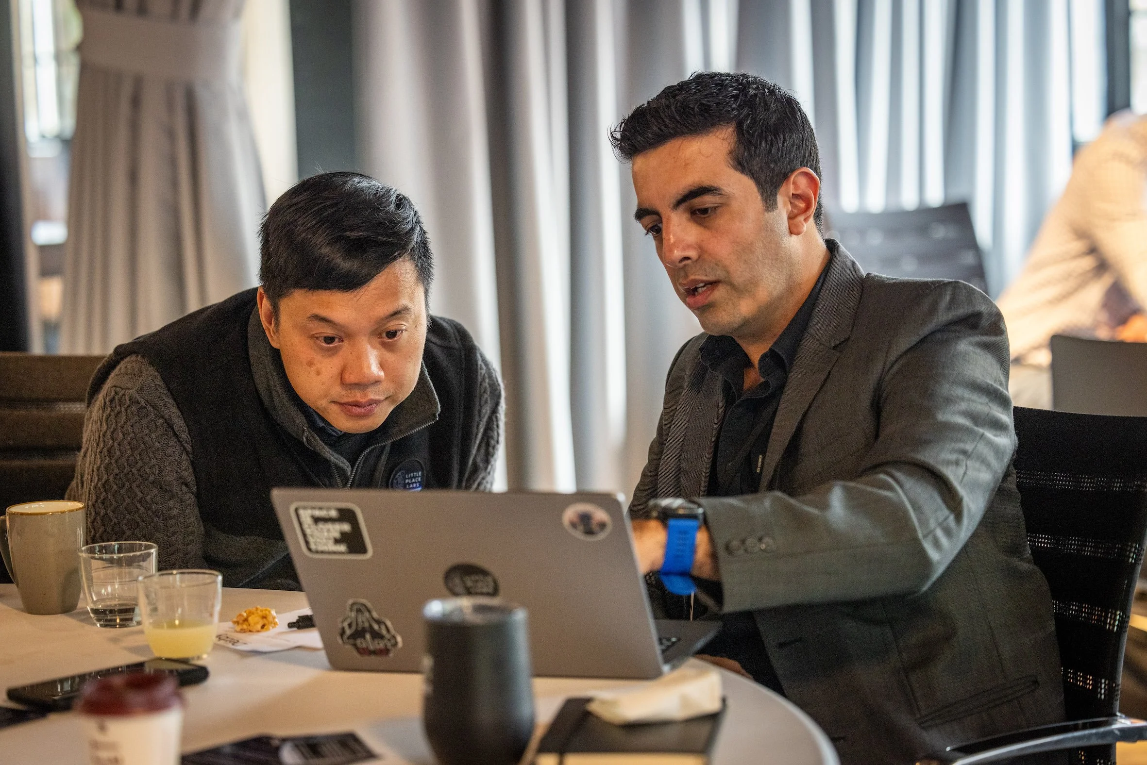 Two men sitting at a table looking at a laptop.