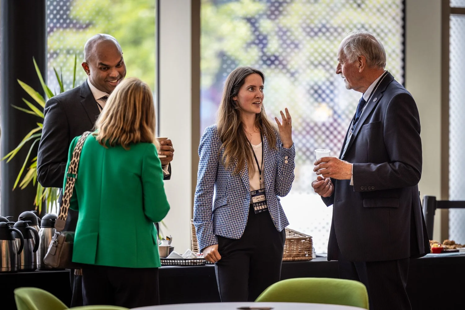 Four people are having a conversation at a networking event. They are dressed in business attire and holding drinks.