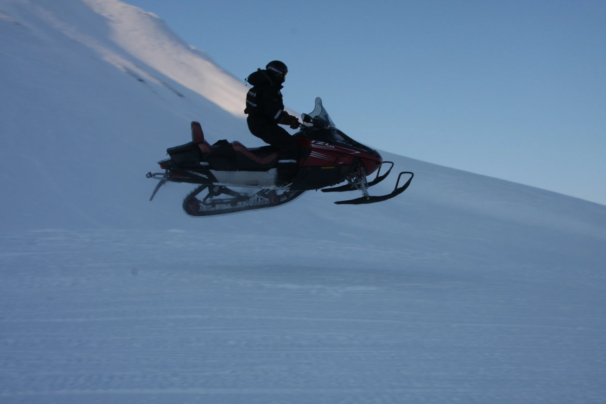 En person kjører snøscooter på snødekt fjell. 