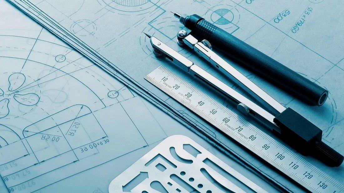 Engineering blueprints with a technical pen, a ruler, and a part   used in drafting.