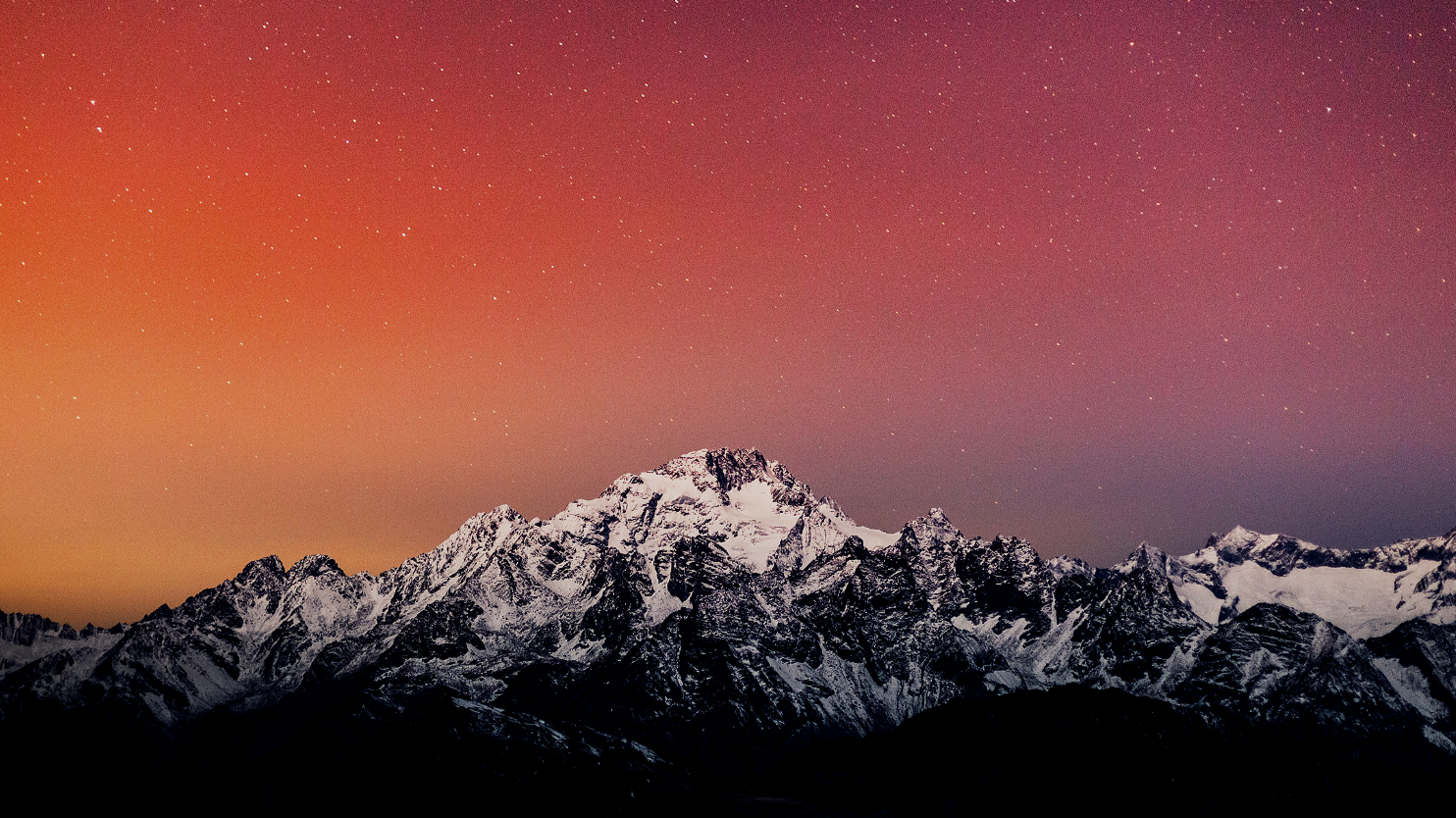 Snow-capped mountain range under a starry sky with a gradient of colors from orange to purple.