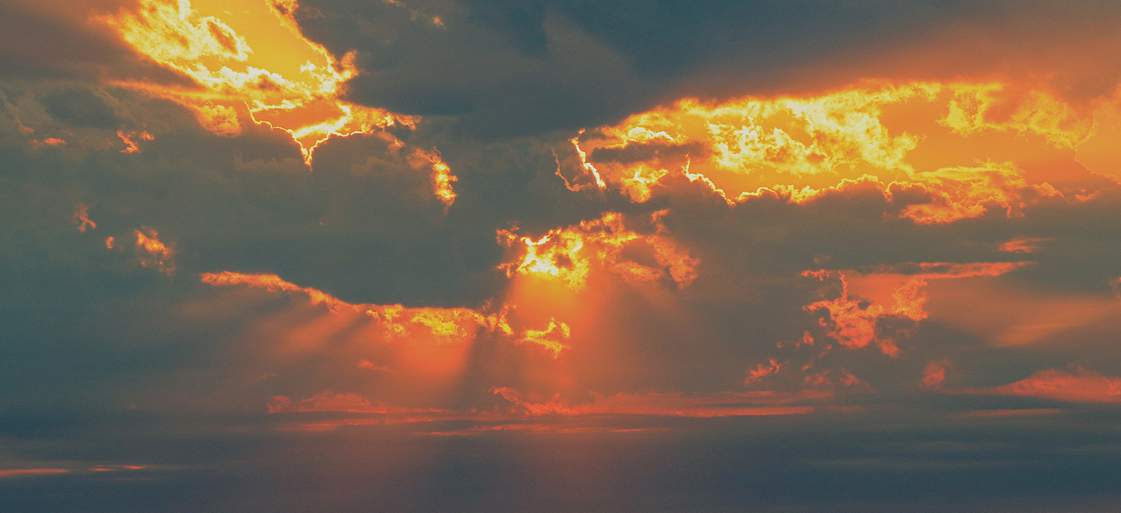 Sunset sky with golden and orange clouds and rays of sunlight breaking through.