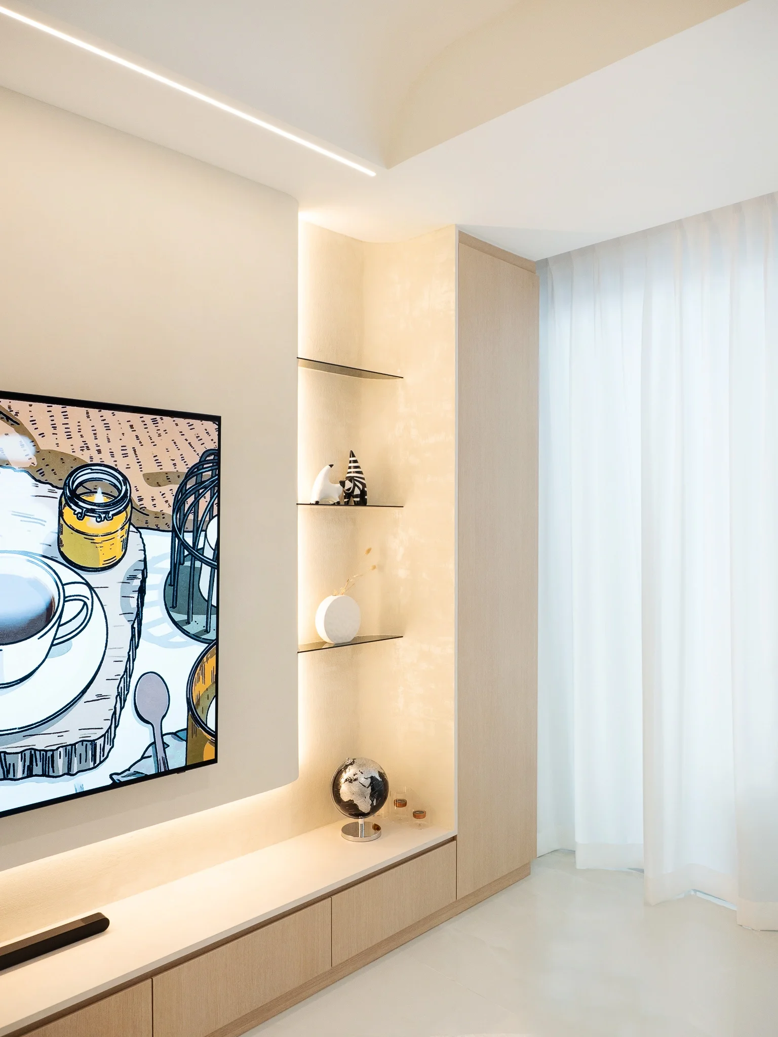 Modern living room with a flat-screen TV, a built-in wooden cabinet with decorative items, and white curtains.
