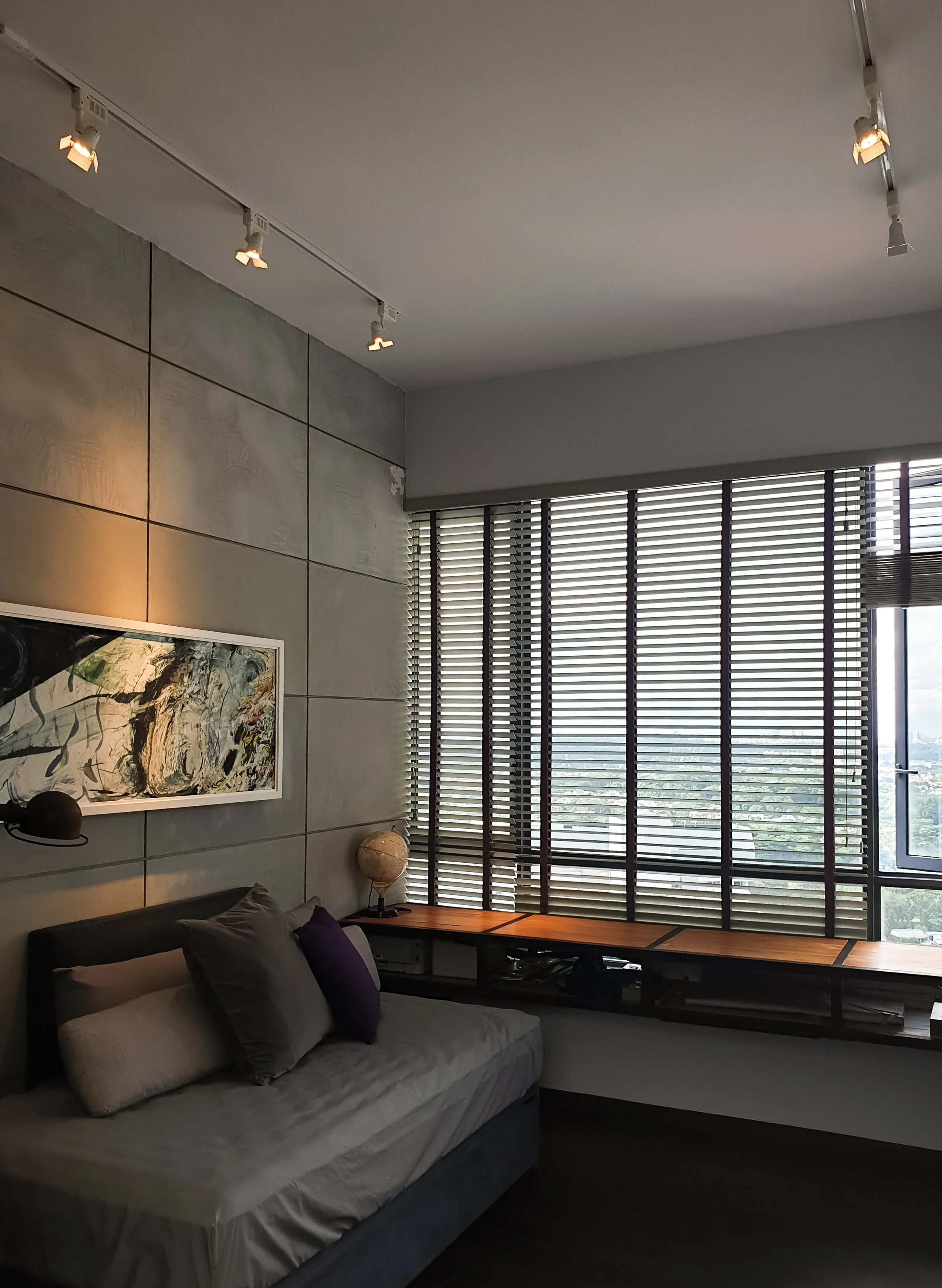 A modern living room with a gray sofa, throw pillows, a globe, and large windows with blinds showing a city view.