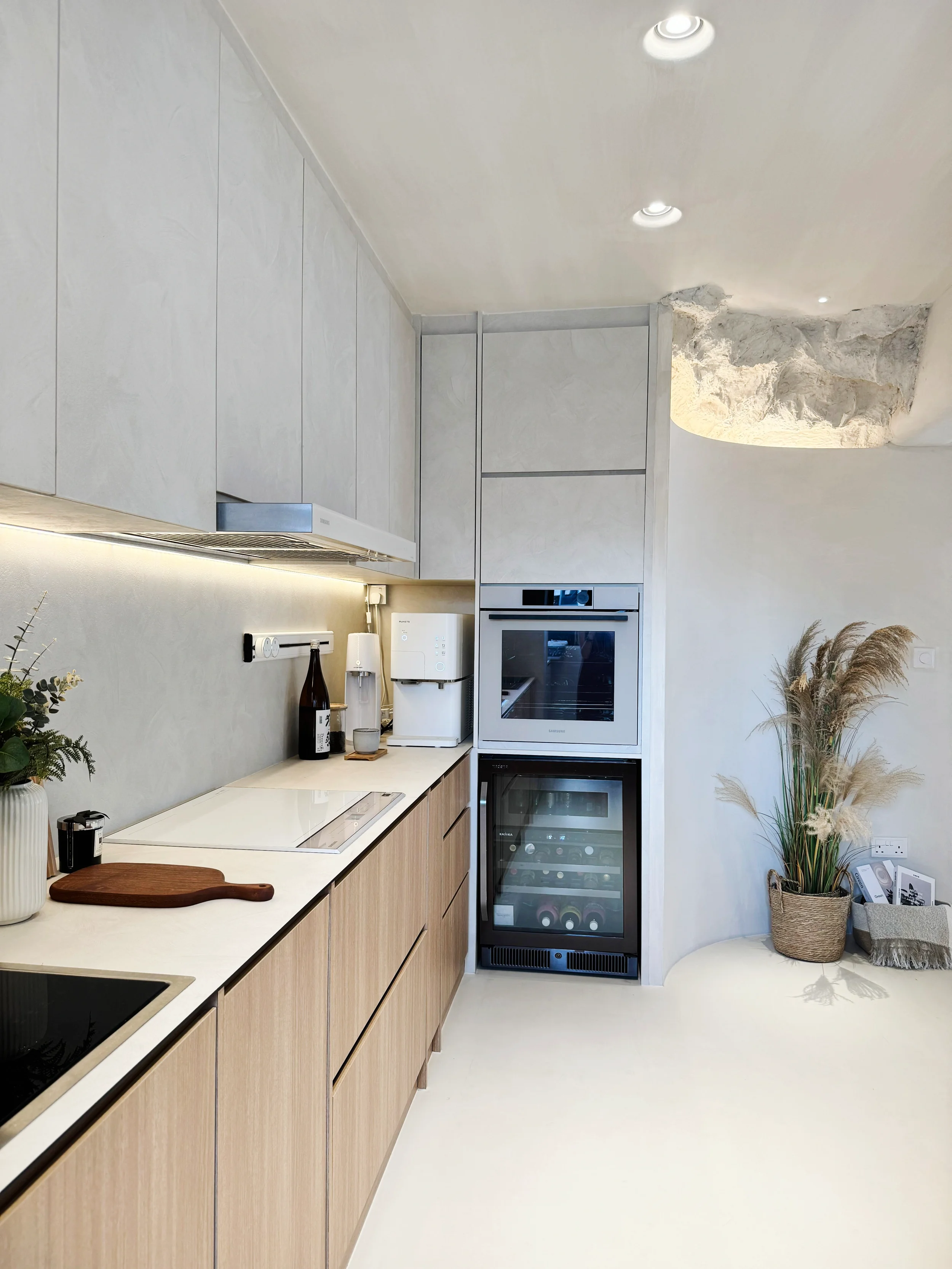 Modern kitchen with light wood cabinetry, white countertops, built-in appliances, potted plant and decorative items.