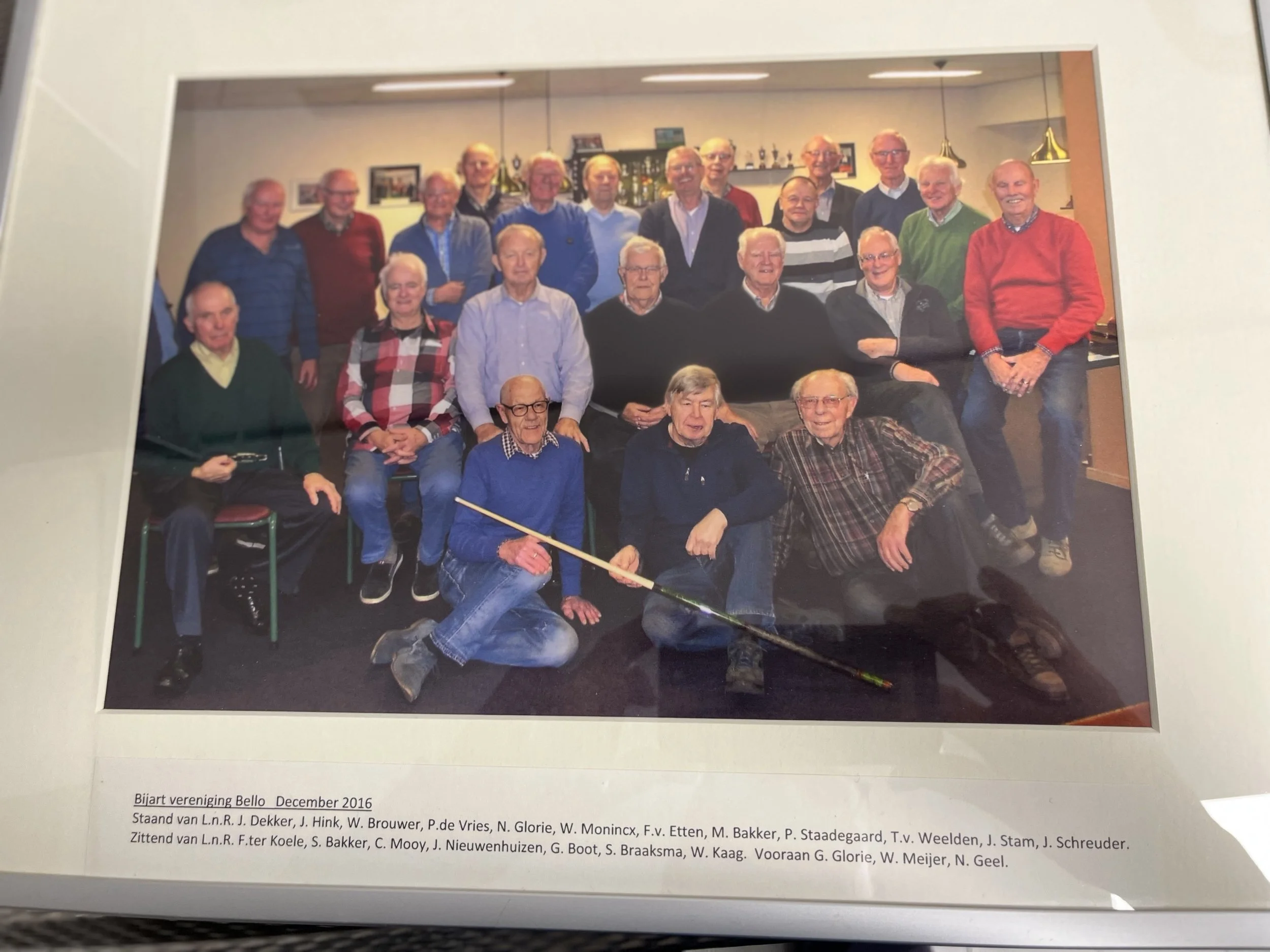 A group of elderly men and women gathered together in a room, posing for a photo, with some seated and others standing behind them.