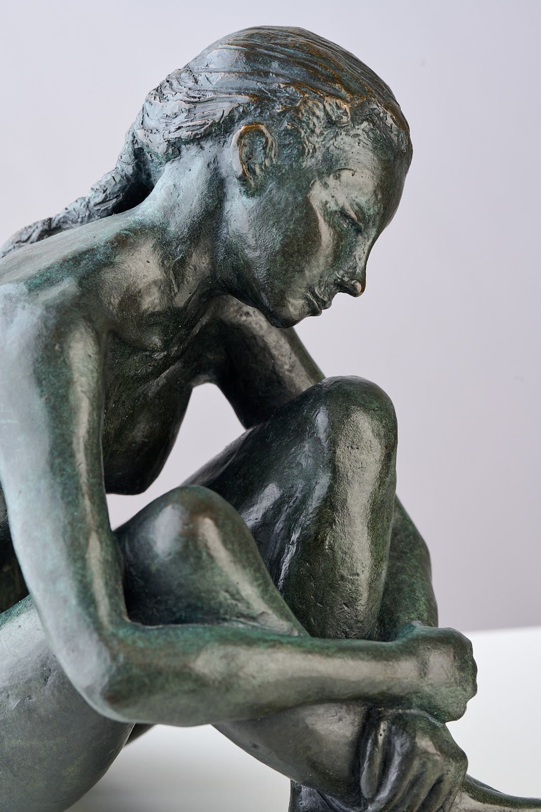 Bronze sculpture of a woman sitting with her head bowed and arms wrapped around her knees.
