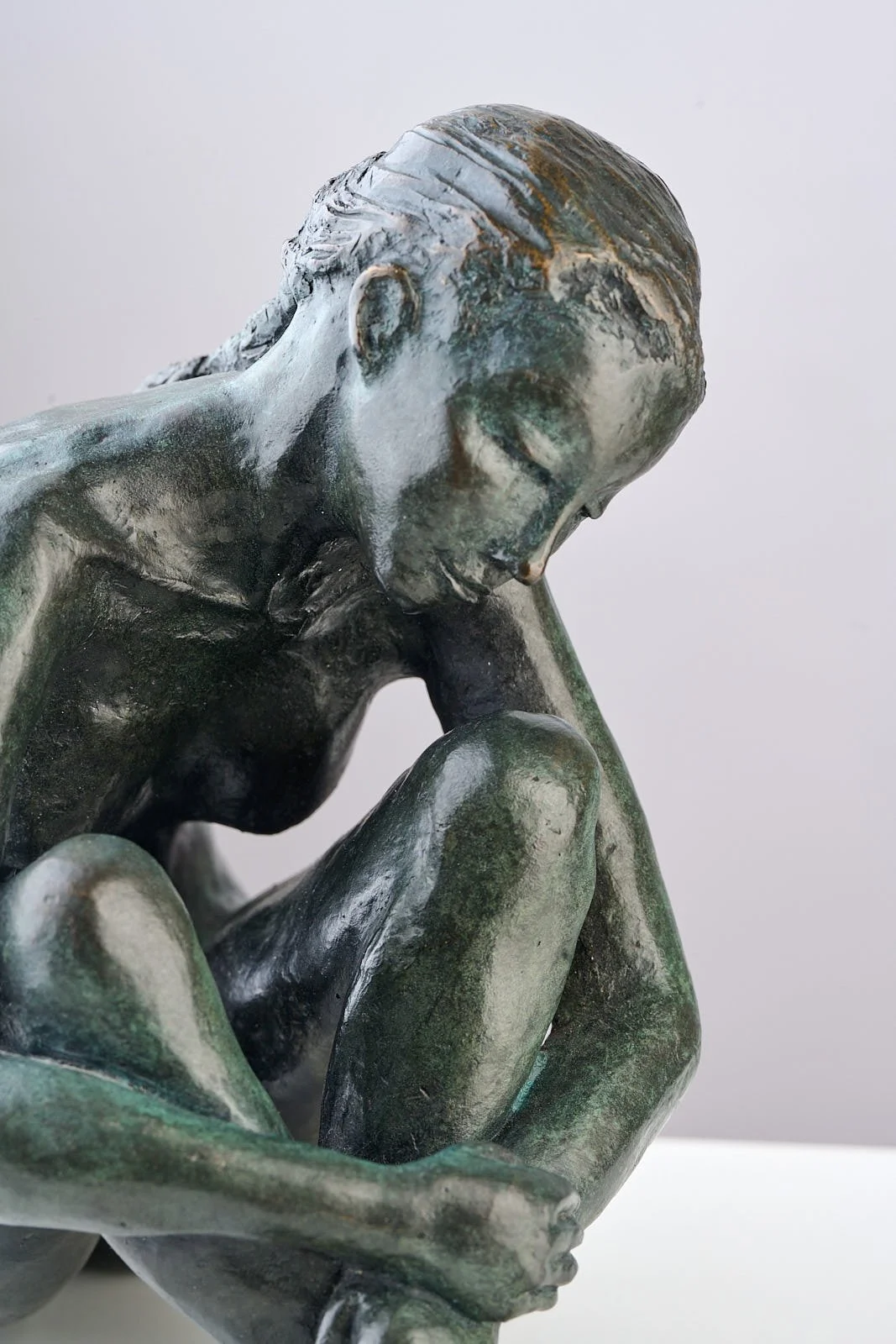 Close-up of a bronze sculpture of a woman sitting with her head bowed and hand on her knee, looking down thoughtfully.