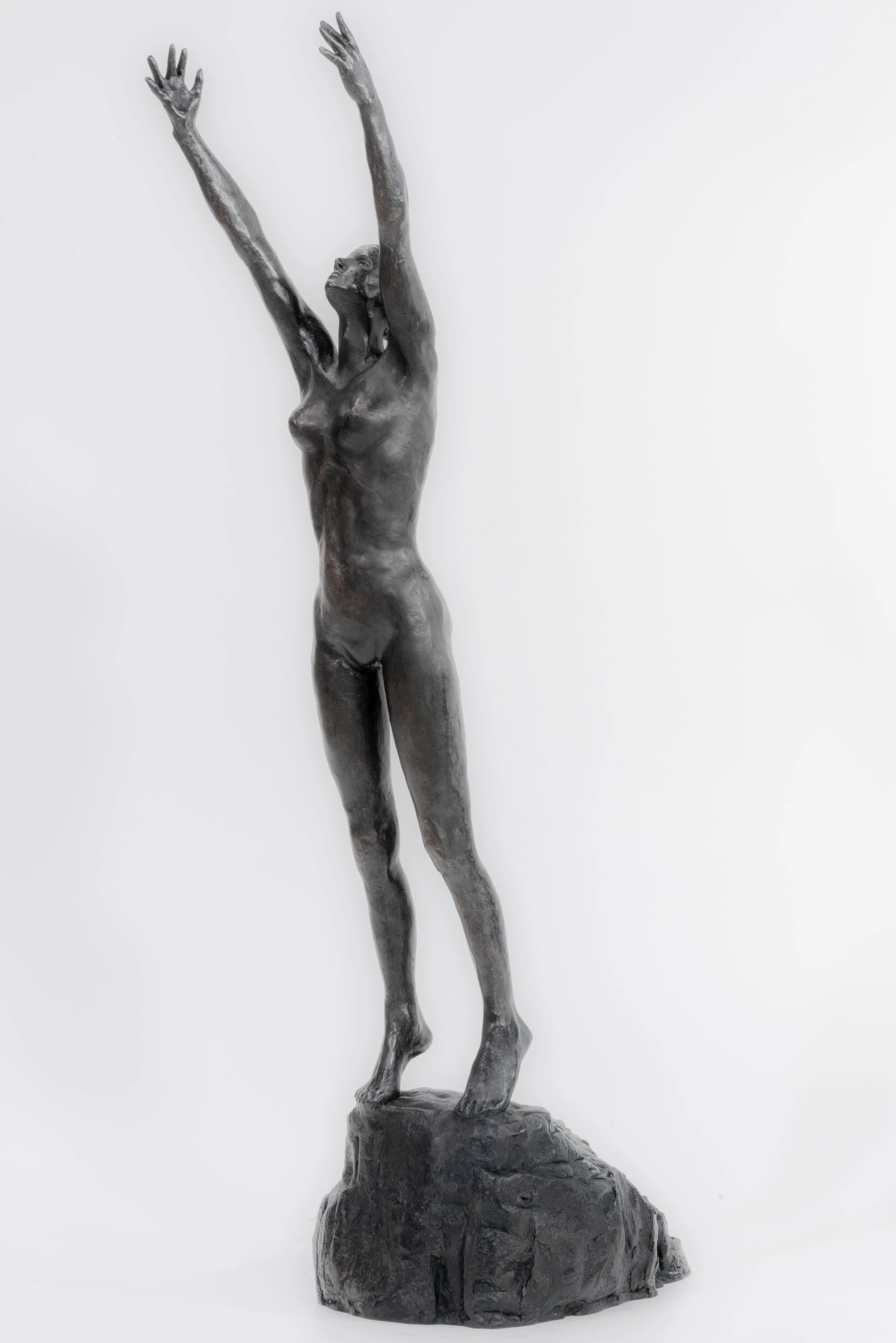 A bronze sculpture of a nude woman standing on a rocky base with arms raised and head tilted back.