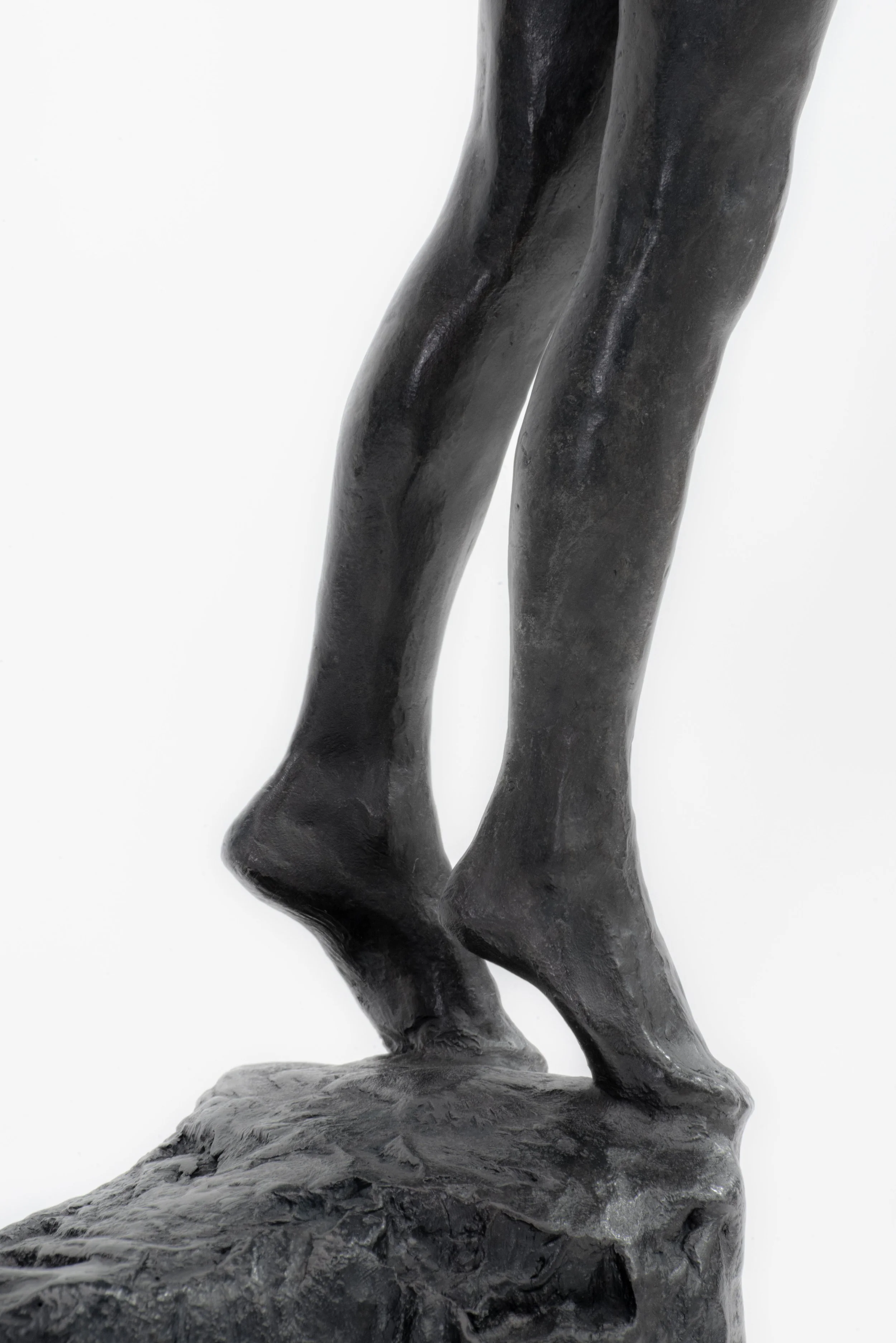 Close-up of a dark bronze sculpture of a person's legs standing on a textured base against a plain white background.