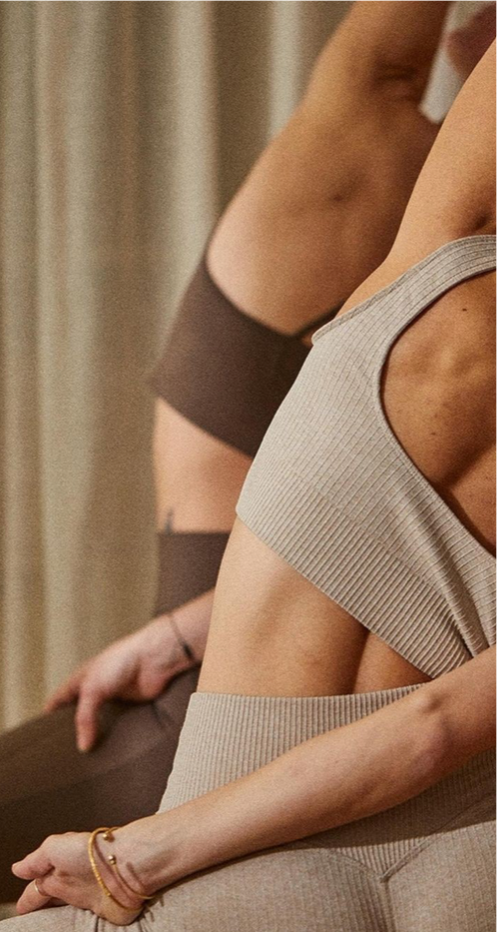 Close-up van vrouwen in sportkleding, zittend met armen omhoog op een reformer, pilates aan het beoefenen.