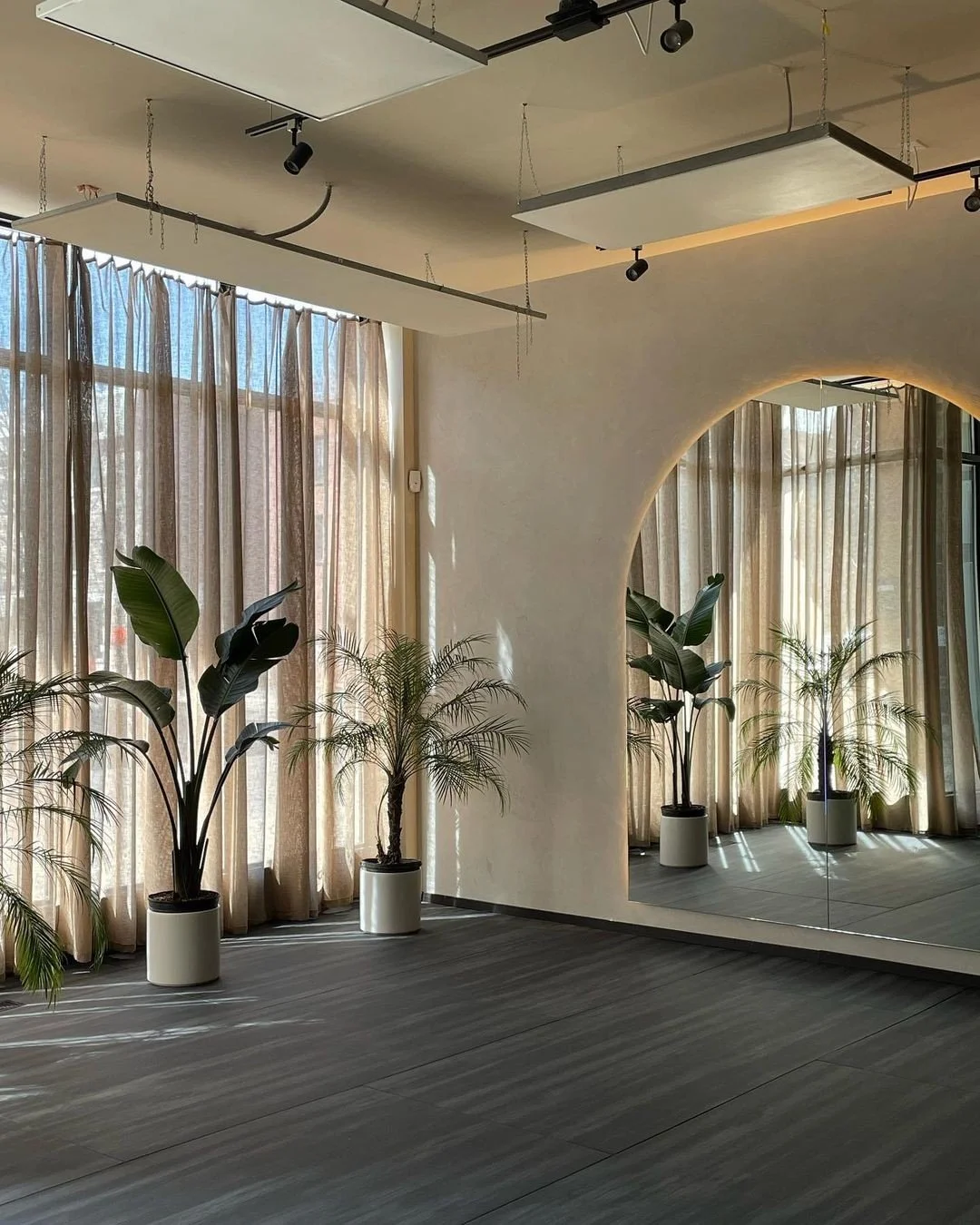 Vier Pilates- of reformer oefenbanken in een lichte, minimalistische ruimte met grote vazen en spiegels.