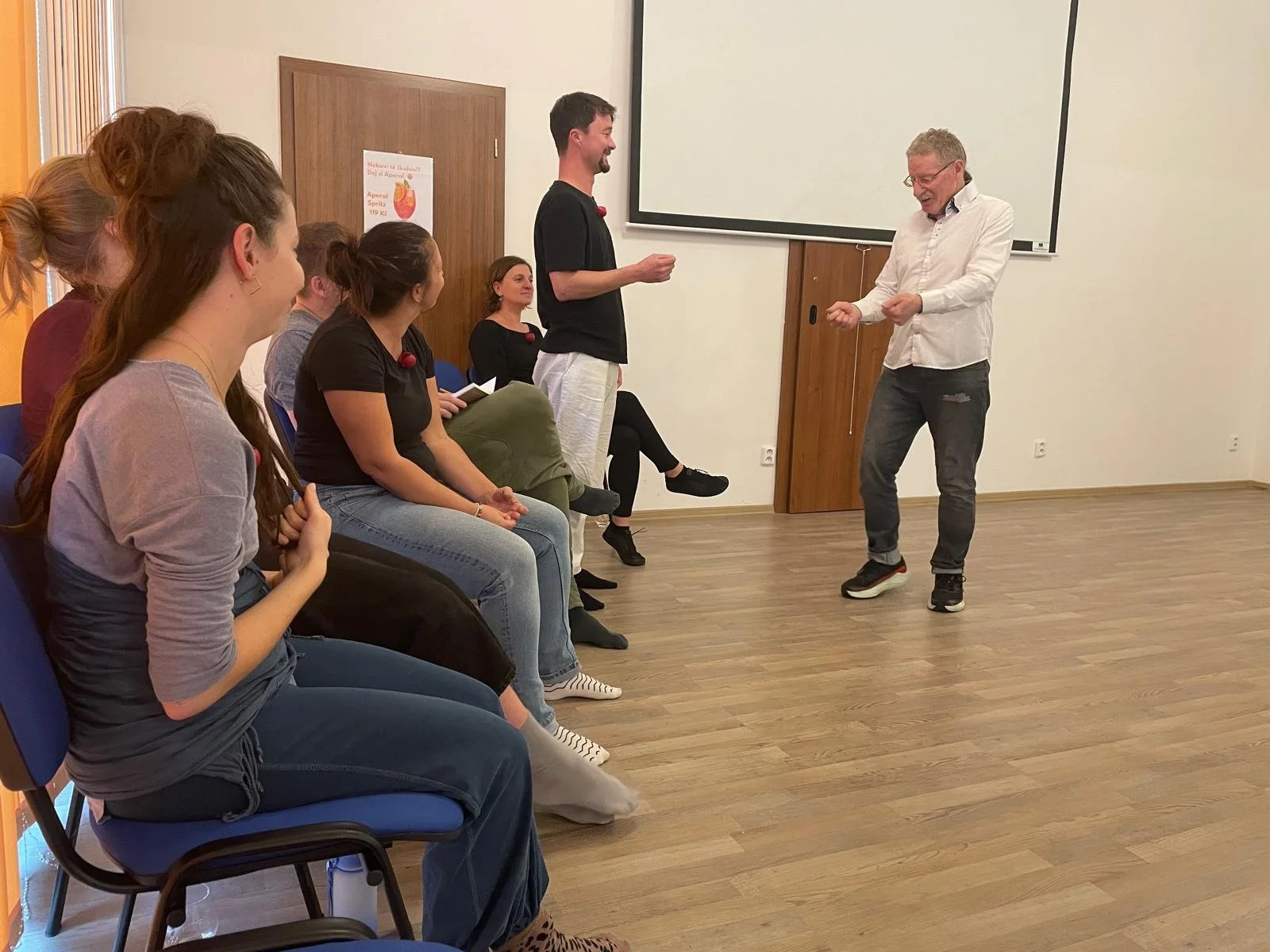 A group of young women sitting and listening to a man standing in front of a whiteboard in a classroom or training room.