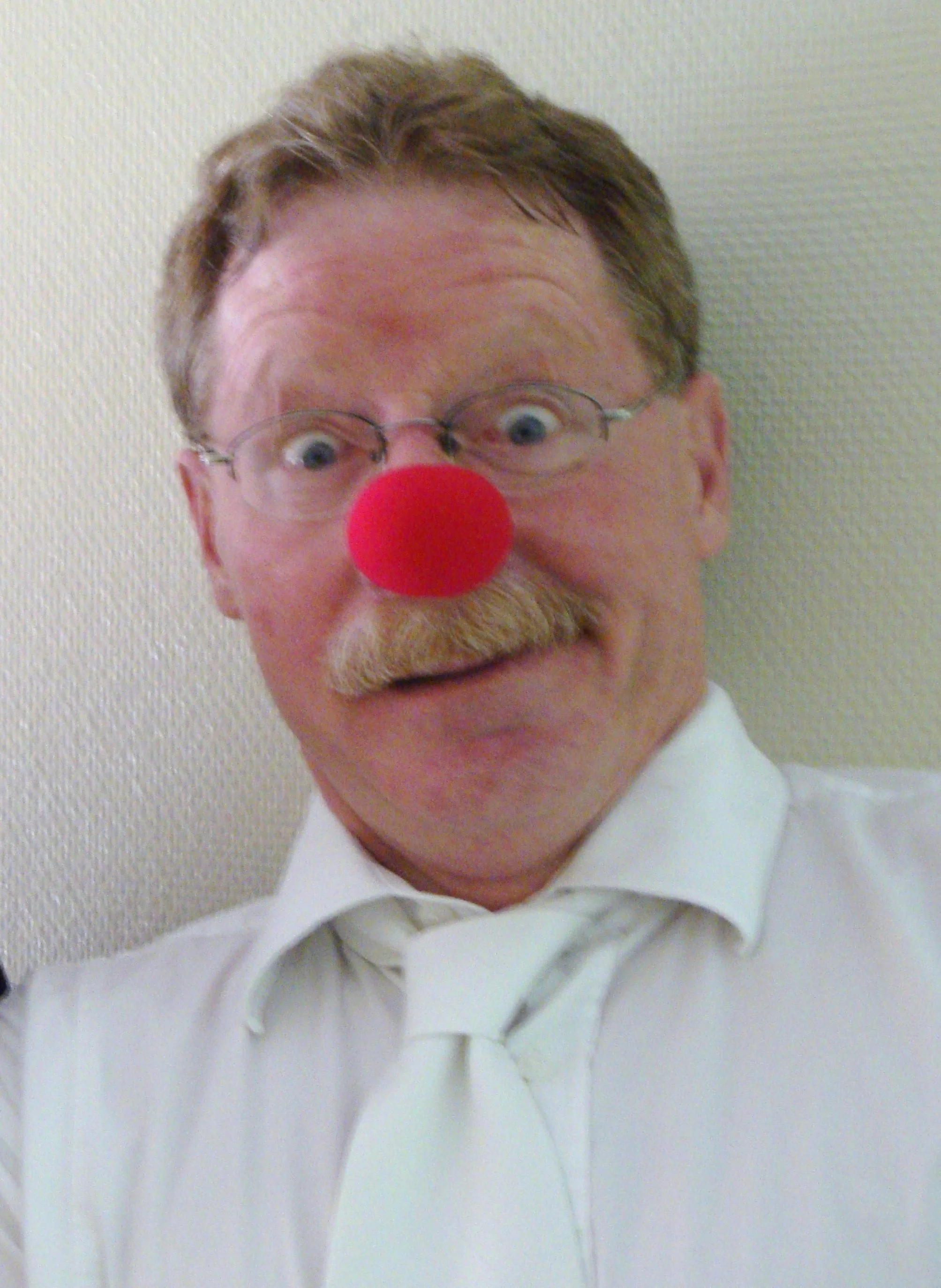 A man with glasses and a red clown nose making a surprised face