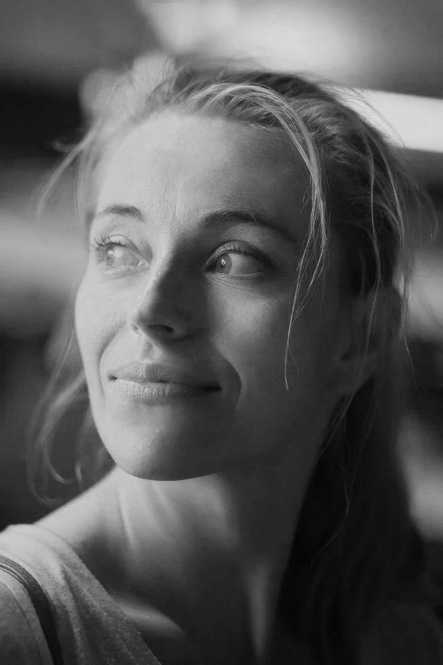 A young woman with light hair looking to the side, smiling softly in black and white.