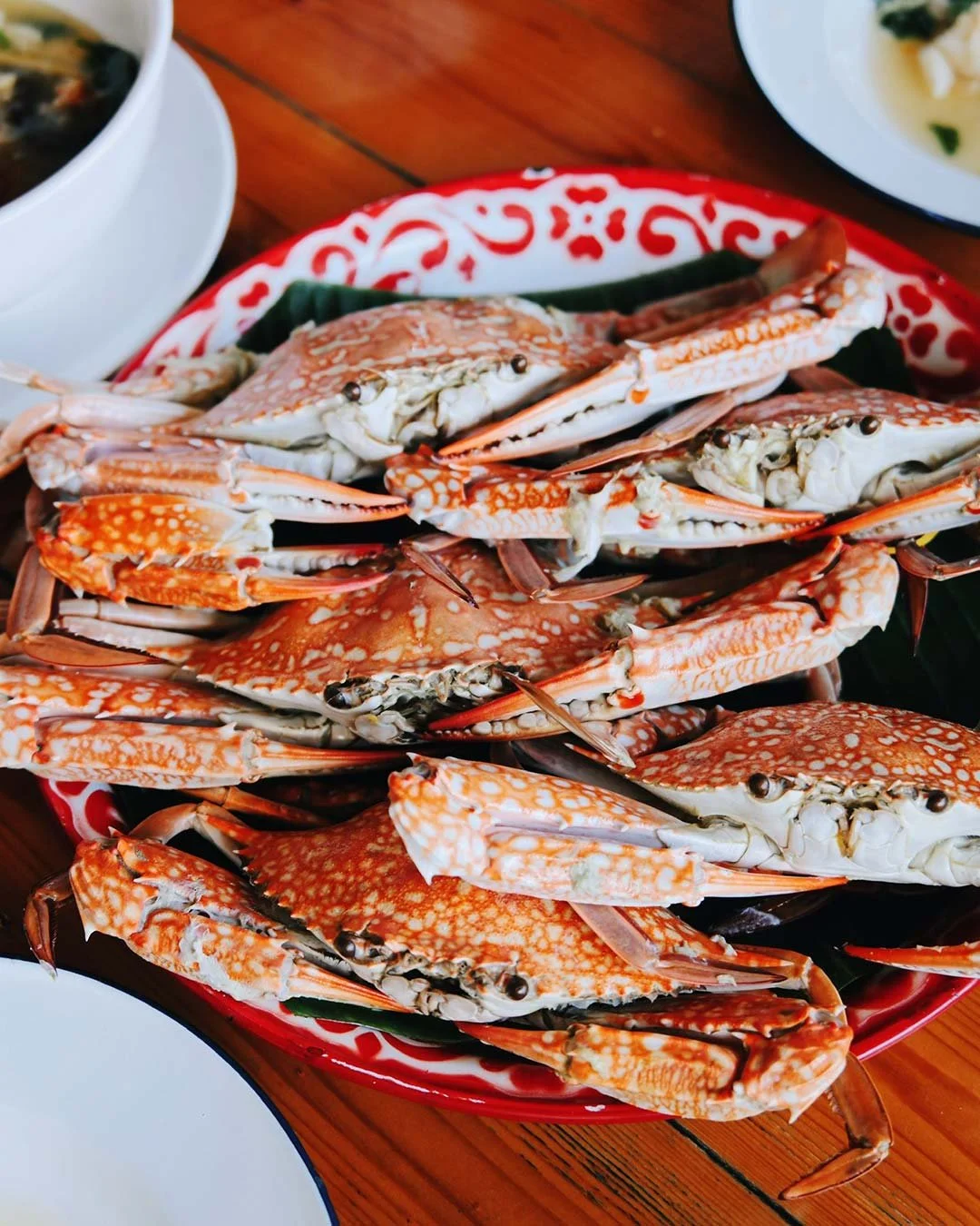 A plate of cooked crabs on a red patterned dish, with some crab claws and shells visible.