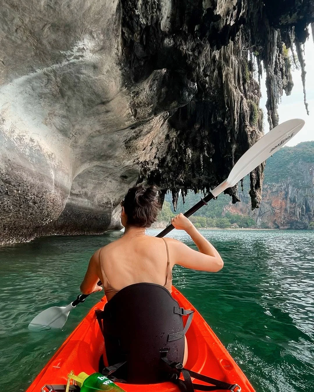Person kayaking near a rocky cave with stalactites at Railay Beach, Thailand
