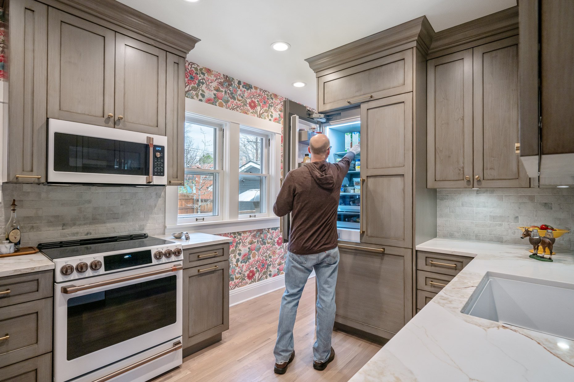 Small Kitchen design with floral wallpaper and light greenish cabinetry. Cafe Appliances and man opening refrigerator