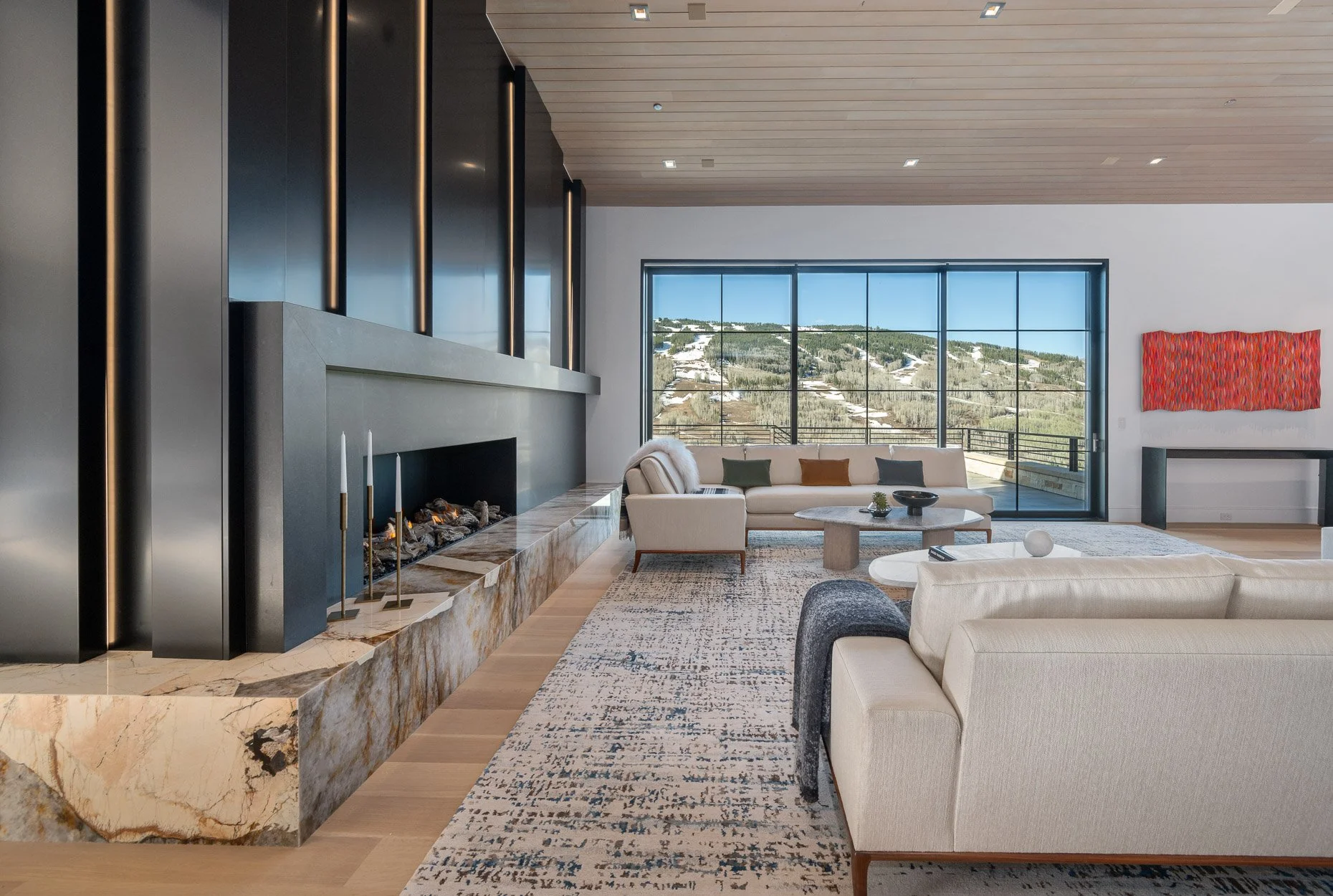 Denver real estate photography - Modern living room with large window view of mountains, white sofas, marble fireplace, and contemporary decor.