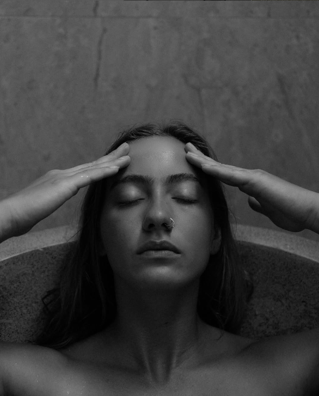 Une femme avec les yeux fermés, tenant sa tête avec ses mains, de face, en noir et blanc.