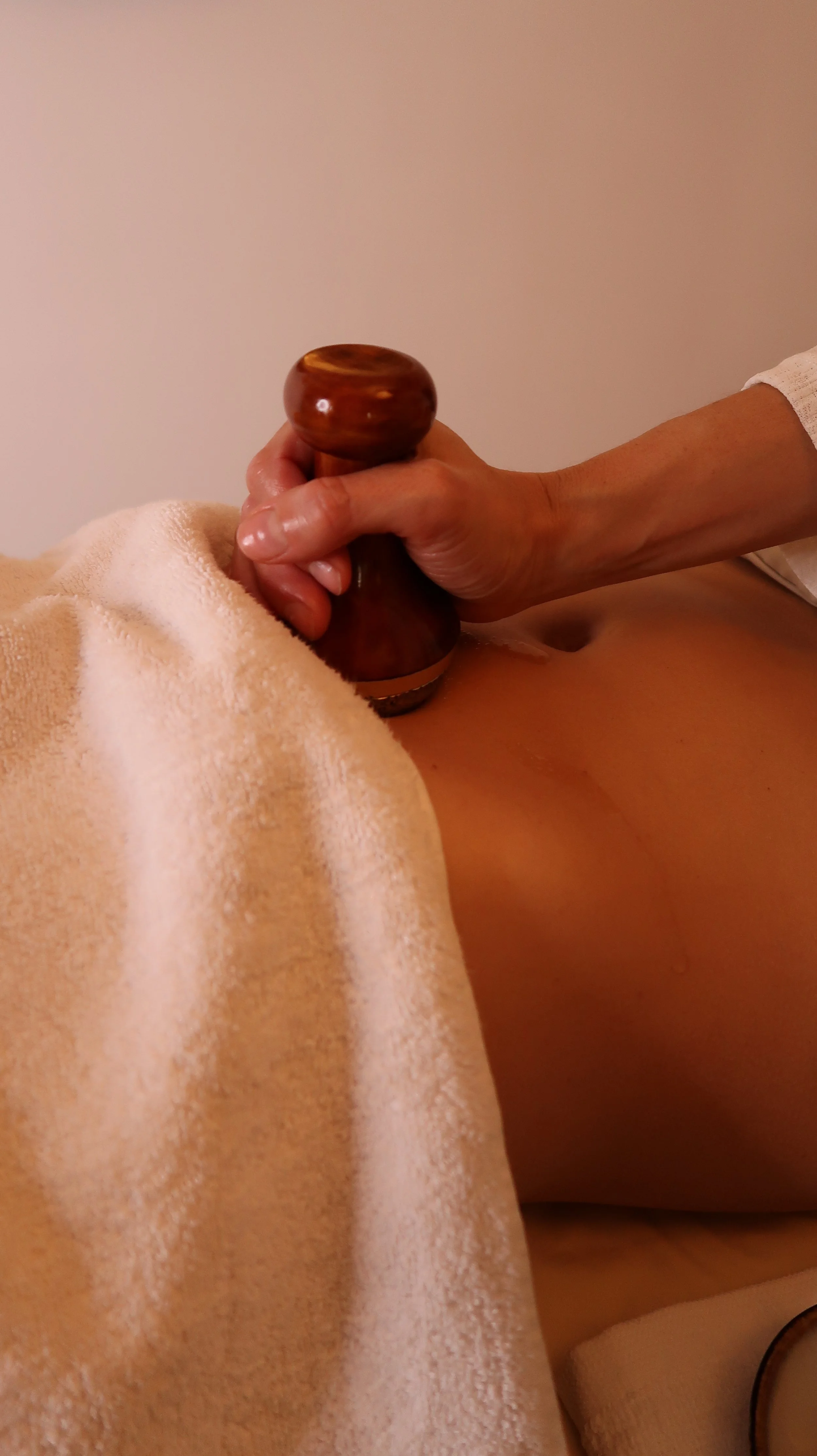 Une personne reçoit un massage avec un outil en bois sur le dos, recouverte d'une serviette beige.